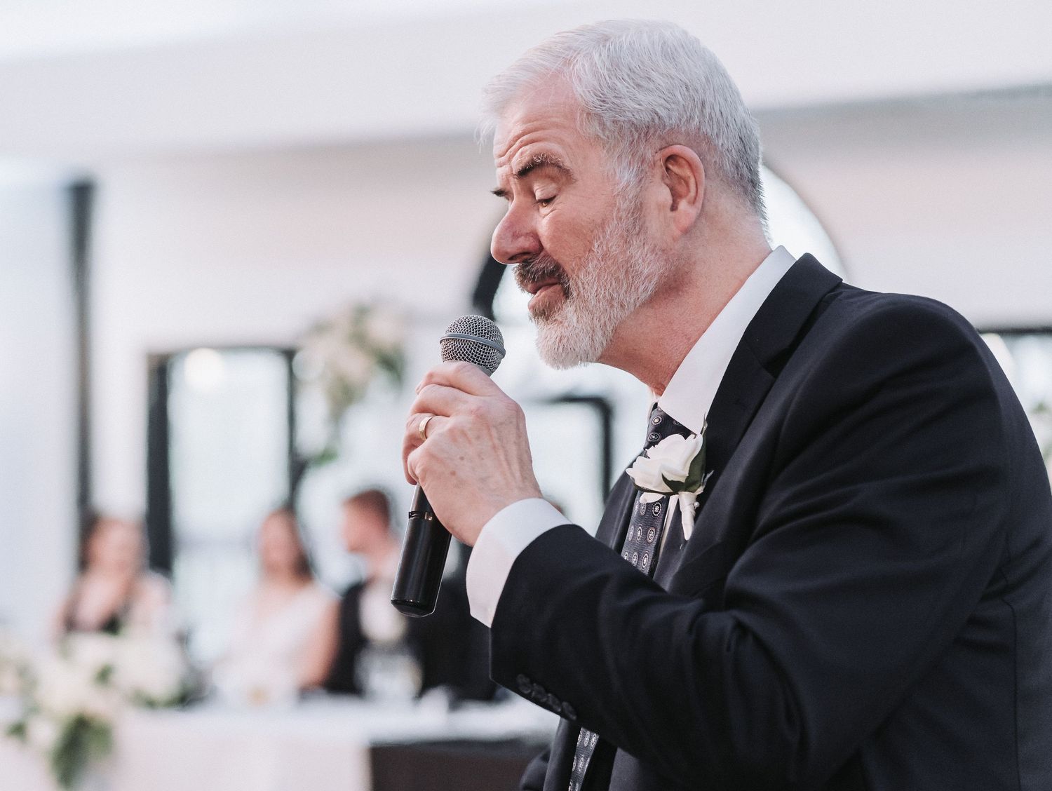 An elderly speaker in a black suit and bow tie delivers a speech into a microphone during a formal event.