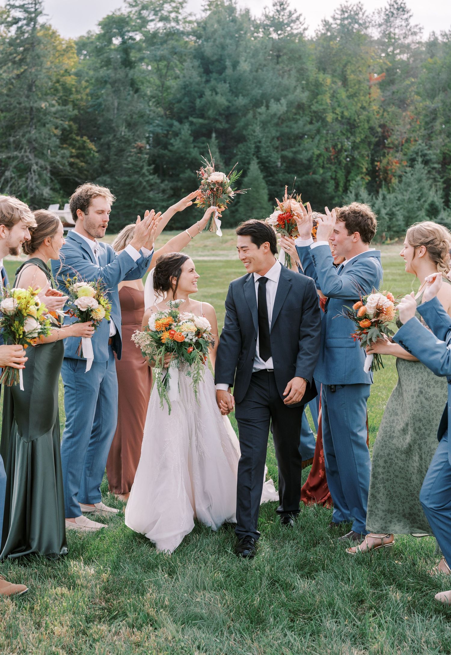 Wedding party arranged in a line outdoors wearing navy suits and earth-toned dresses.