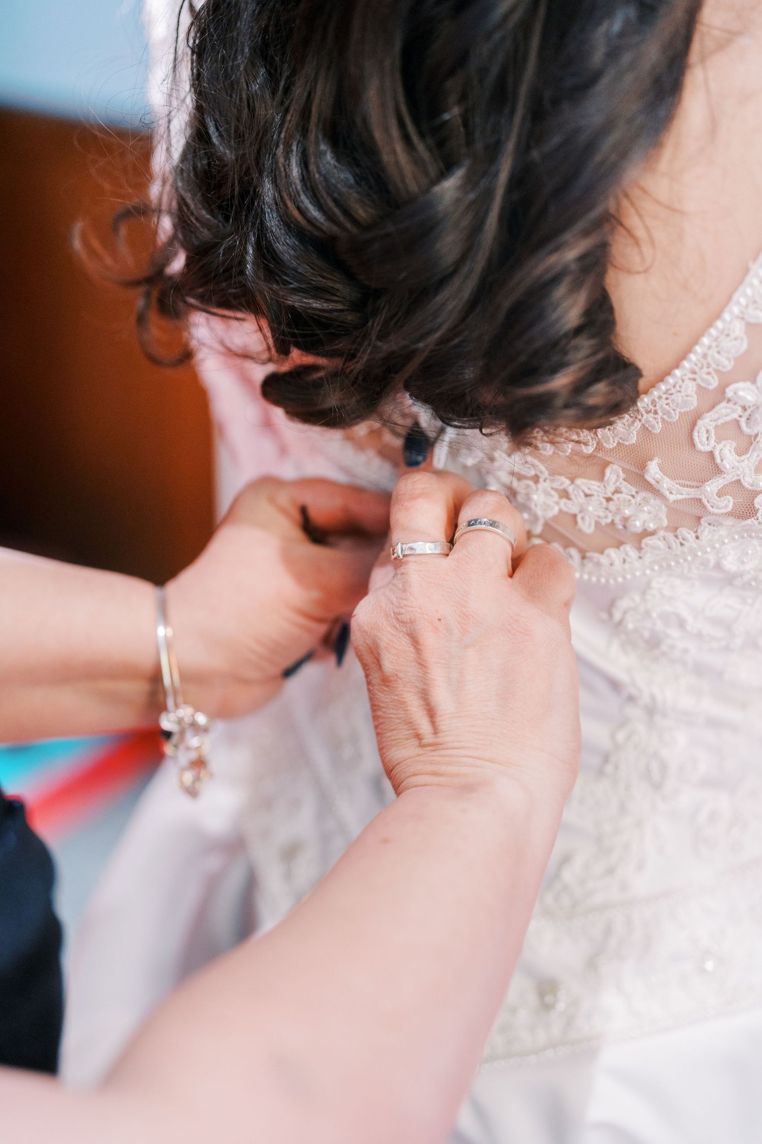 Close-up shots of someone fastening the back buttons of an ornate wedding dress.