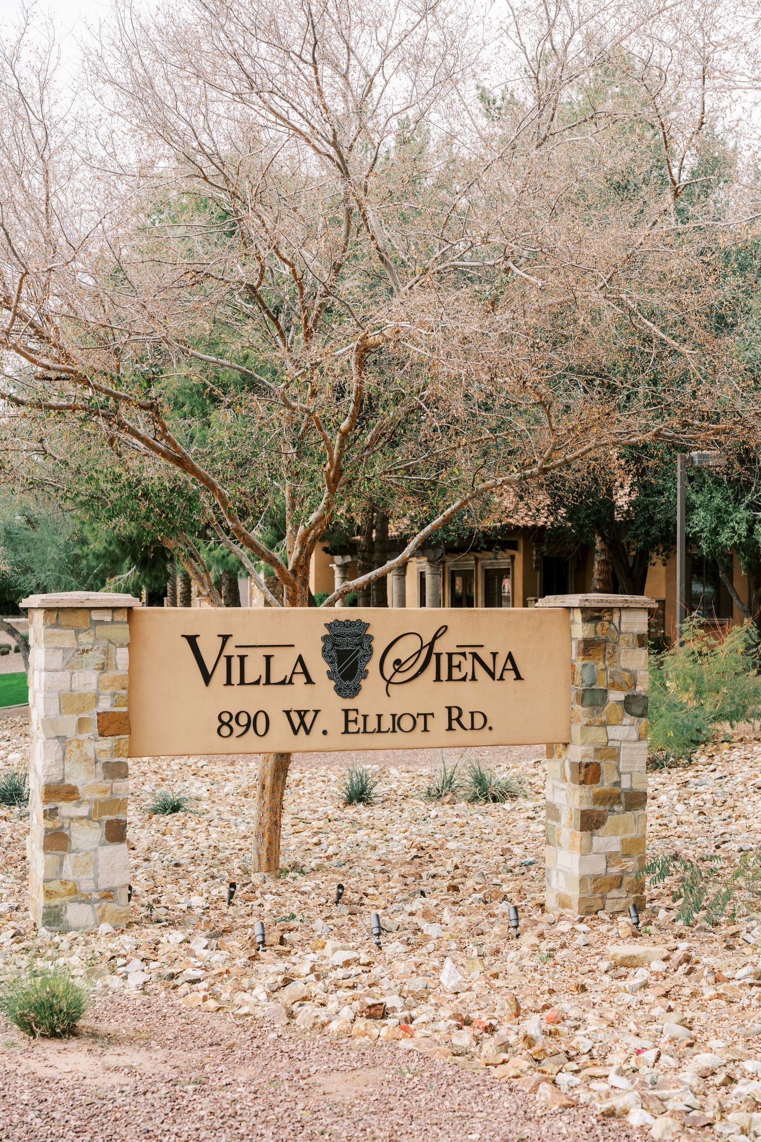 Stone wall entrance sign for Villa Siena at 890 W. Elliot Rd. with desert landscaping and bare winter trees.