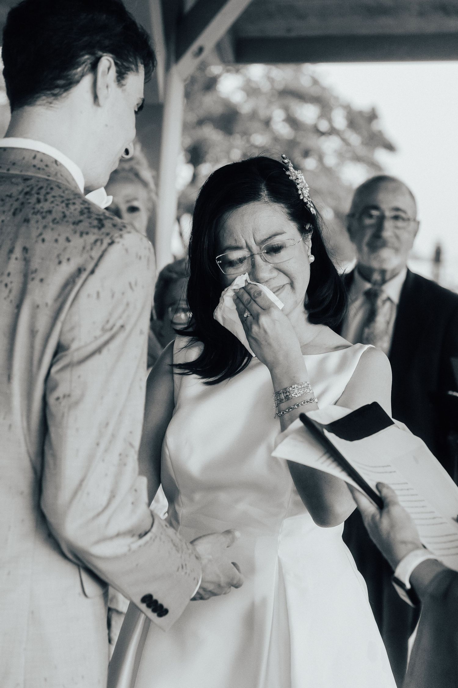 Black and white emotional wedding ceremony moment showing bride wiping away happy tears during the vows.