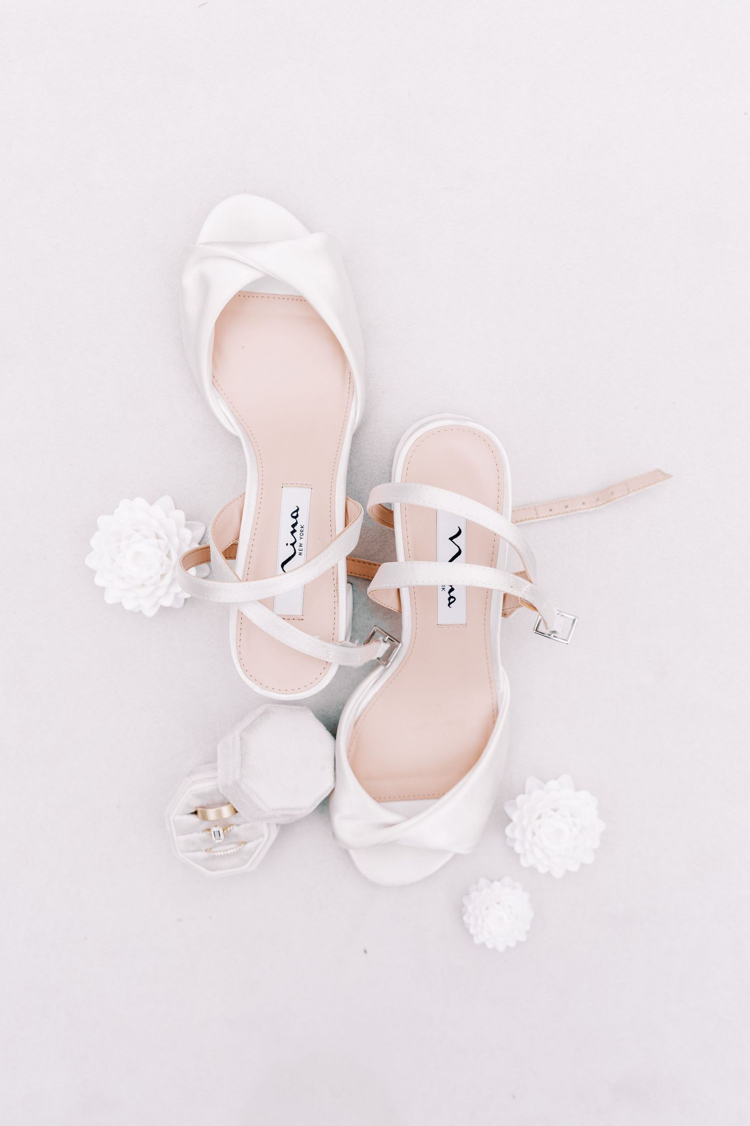 Elegant white bridal shoes with delicate pom pom accessories arranged on light background.