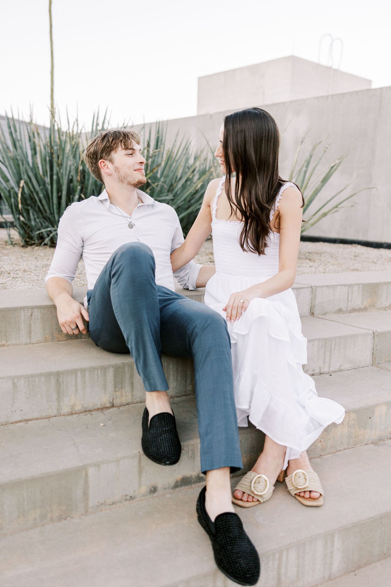 Couple relaxing on concrete steps in casual elegant attire during a photo session.
