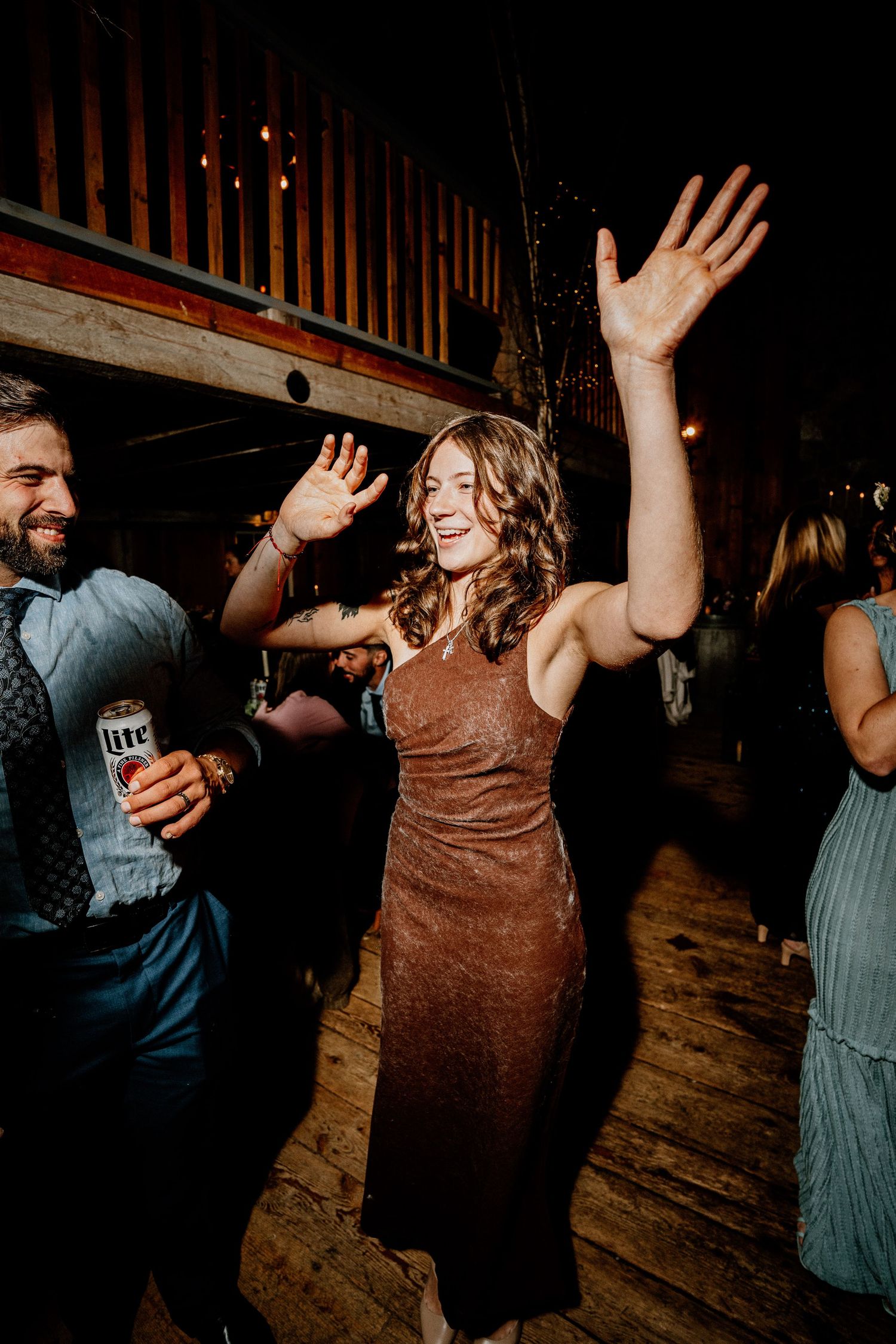 People dancing and raising their hands on a wooden dance floor in a dimly lit venue.
