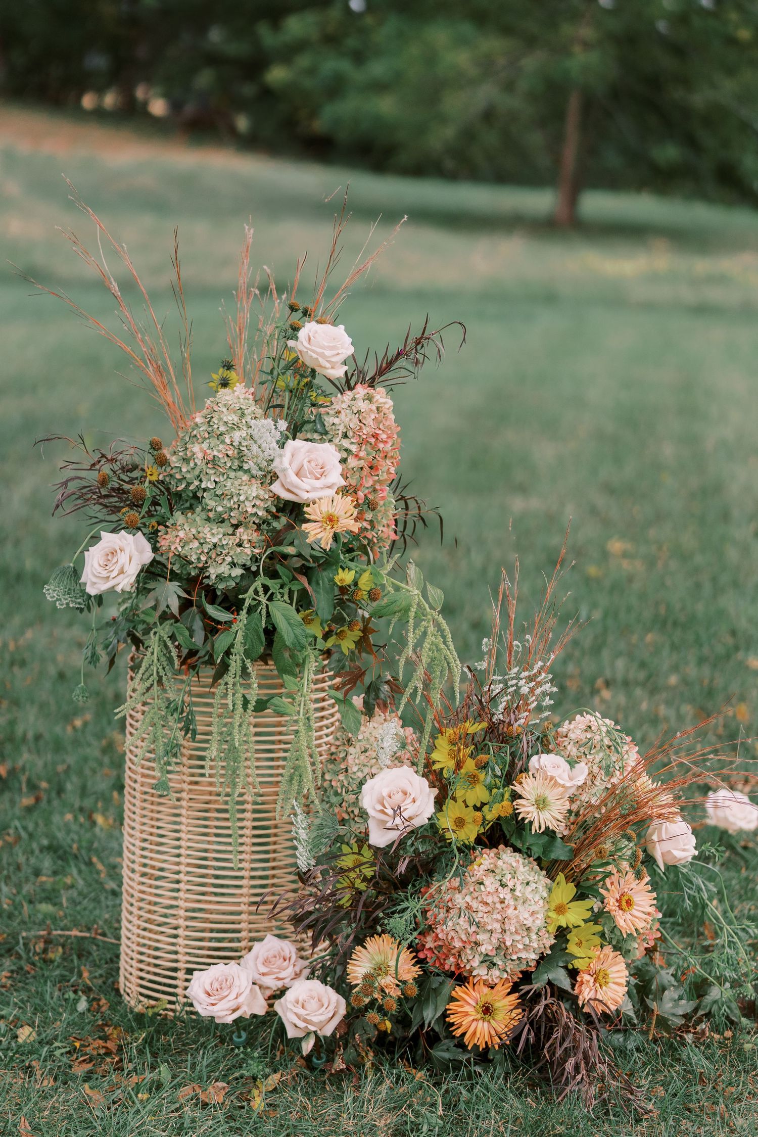 Rustic woven baskets filled with pink roses, dahlias, and wildflowers arranged on green grass.