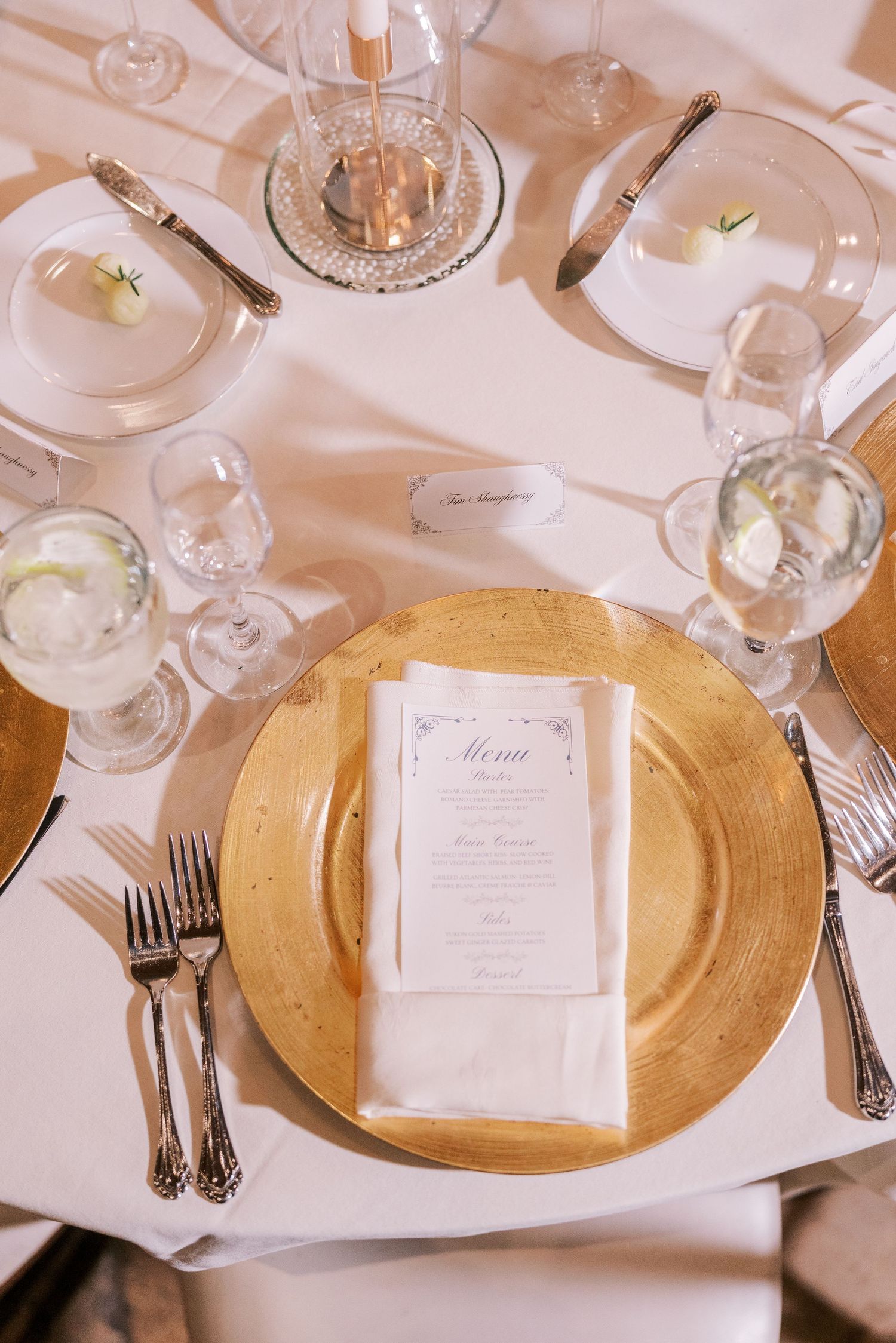 Elegant table settings with gold charger plates and white napkins at a formal dinner event.