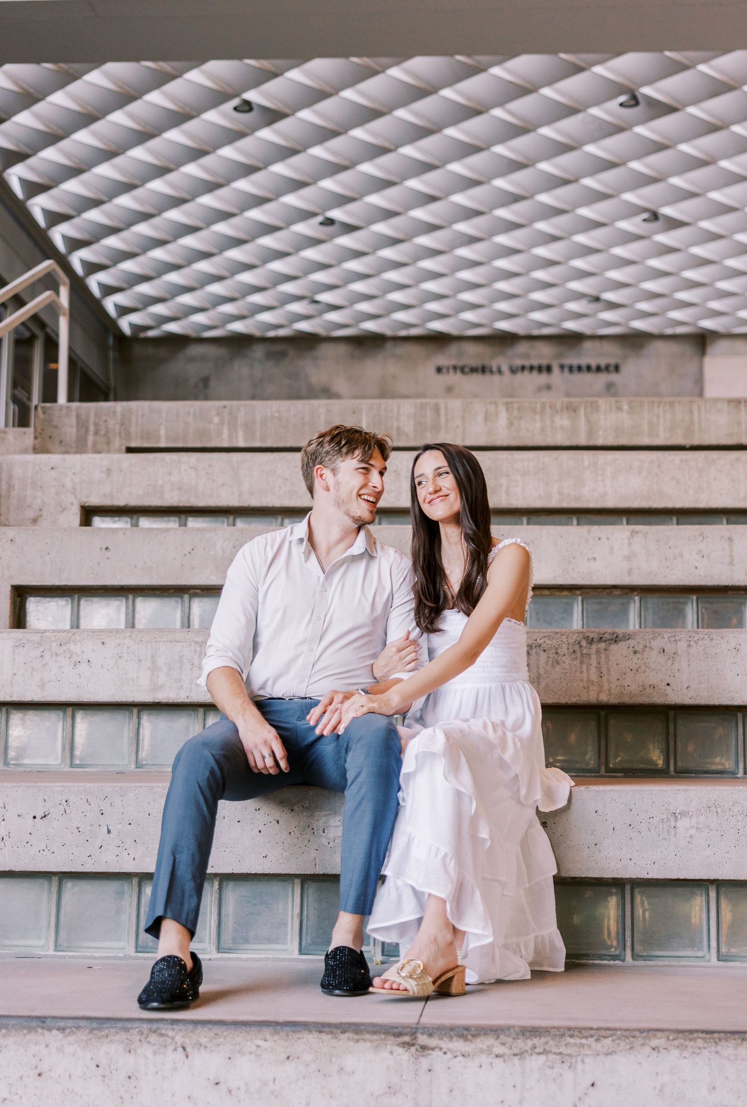 Couple sitting together on concrete stadium steps in a playful and romantic pose.
