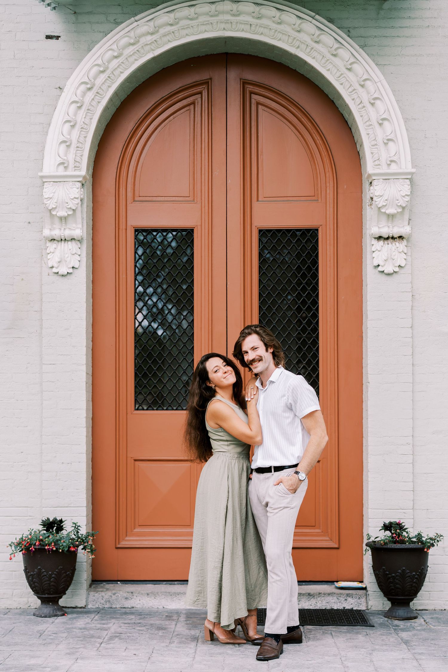 Romantic couple poses by ornate terracotta doors with architectural details.