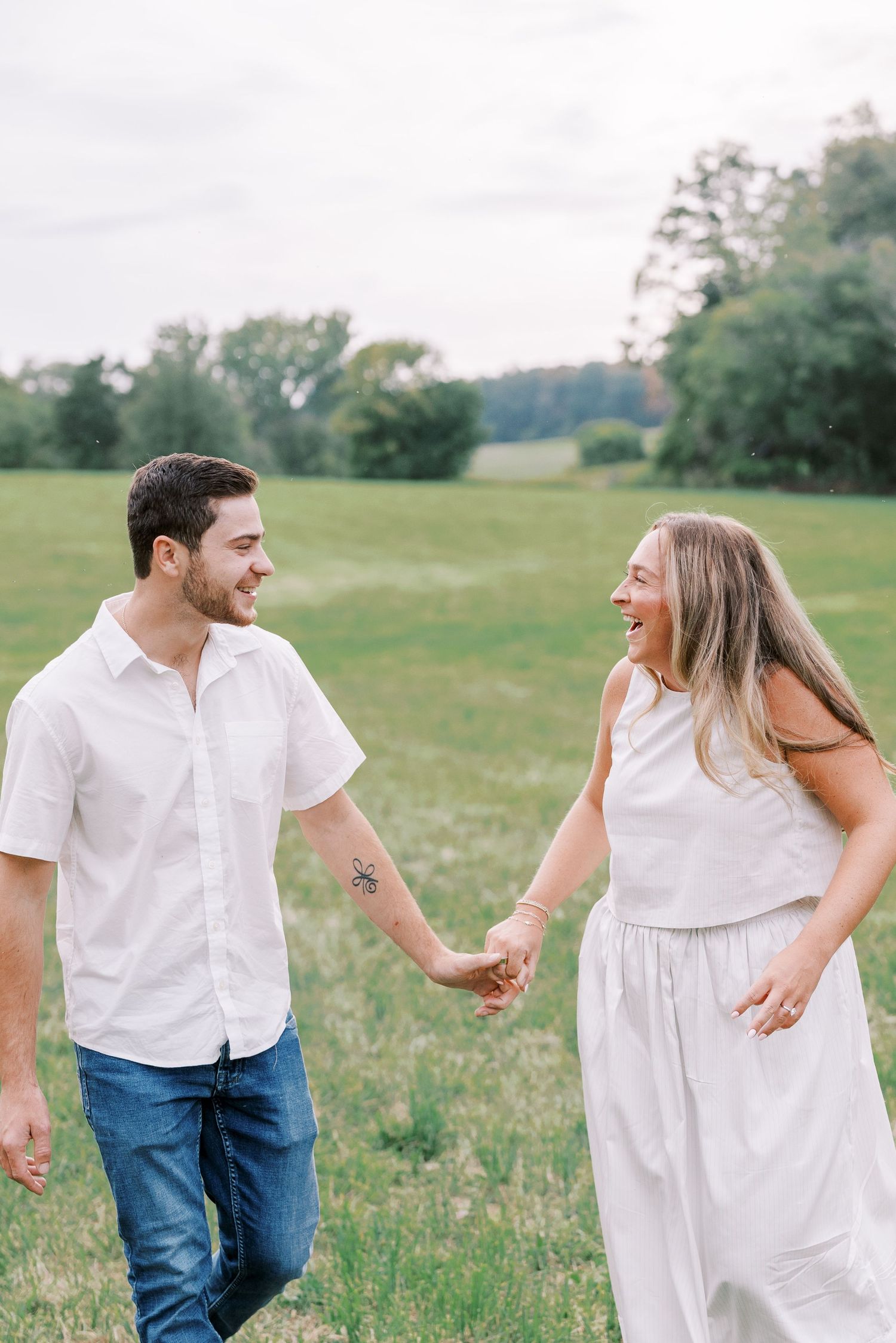 Happy couple holding hands while walking through green summer field.