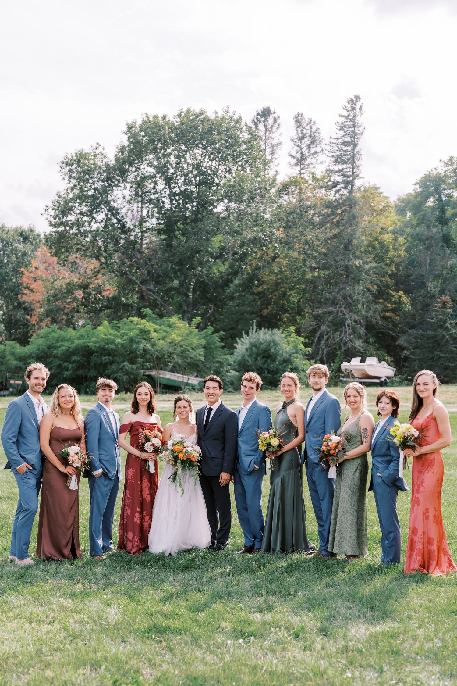 Wedding party members lined up in colorful dresses and suits on a grassy field during an outdoor celebration.