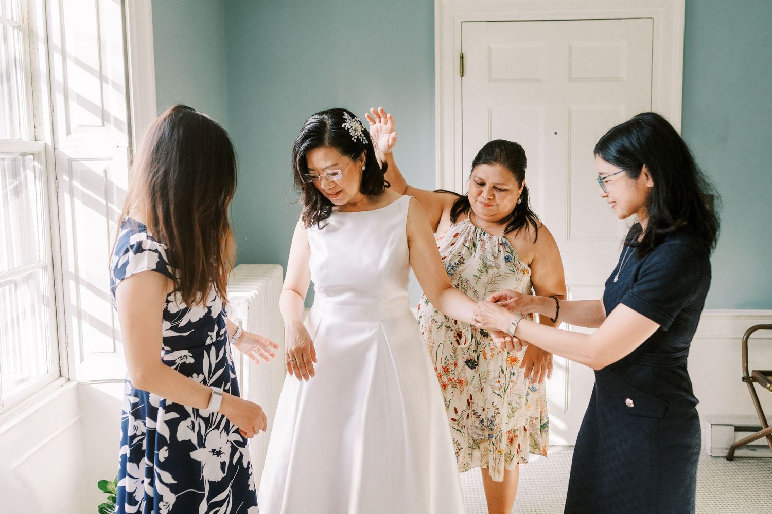 Wedding preparation scene in a bright room as friends help with final dress adjustments.