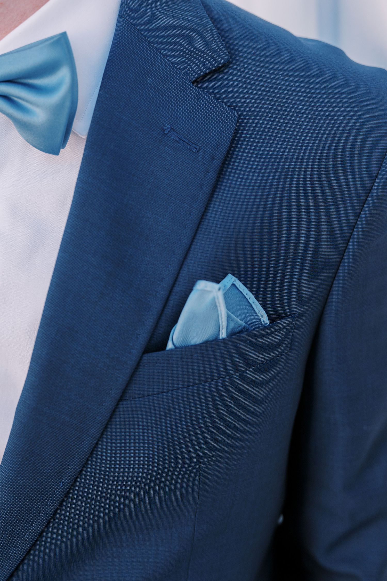 Close-up view of a navy blue suit jacket with light blue pocket square showing subtle fabric texture details.