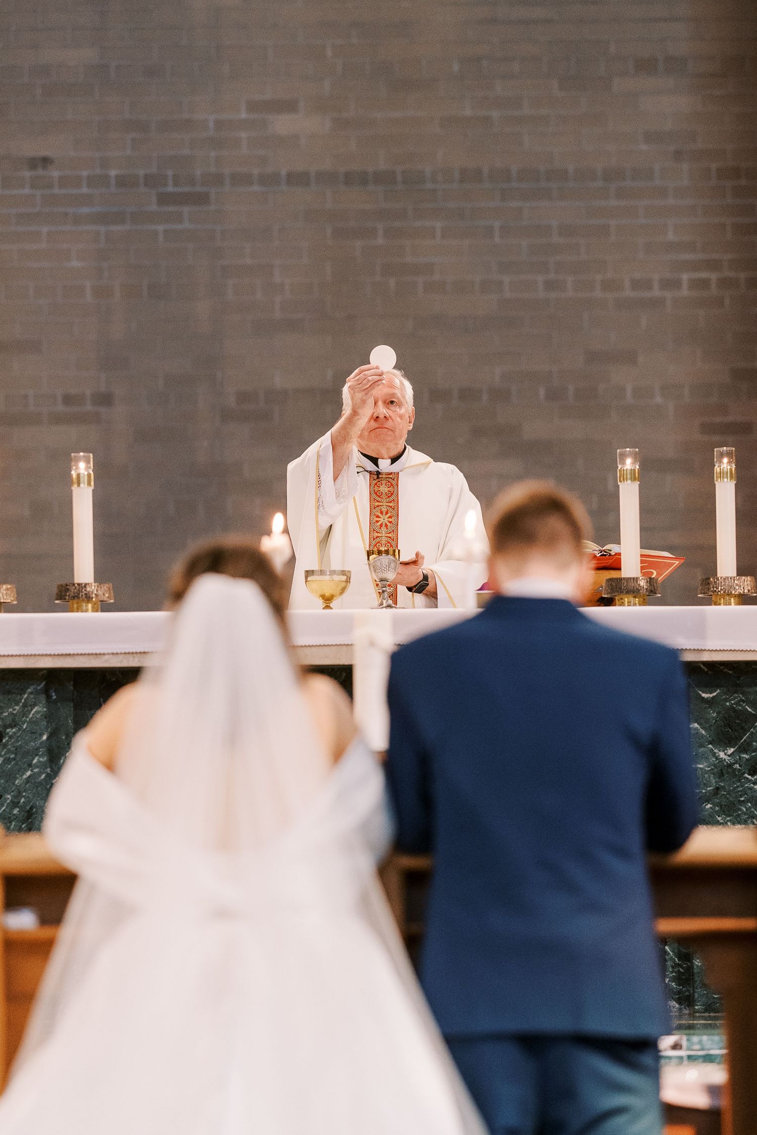 A couple in wedding attire kneels before an altar during their church ceremony.