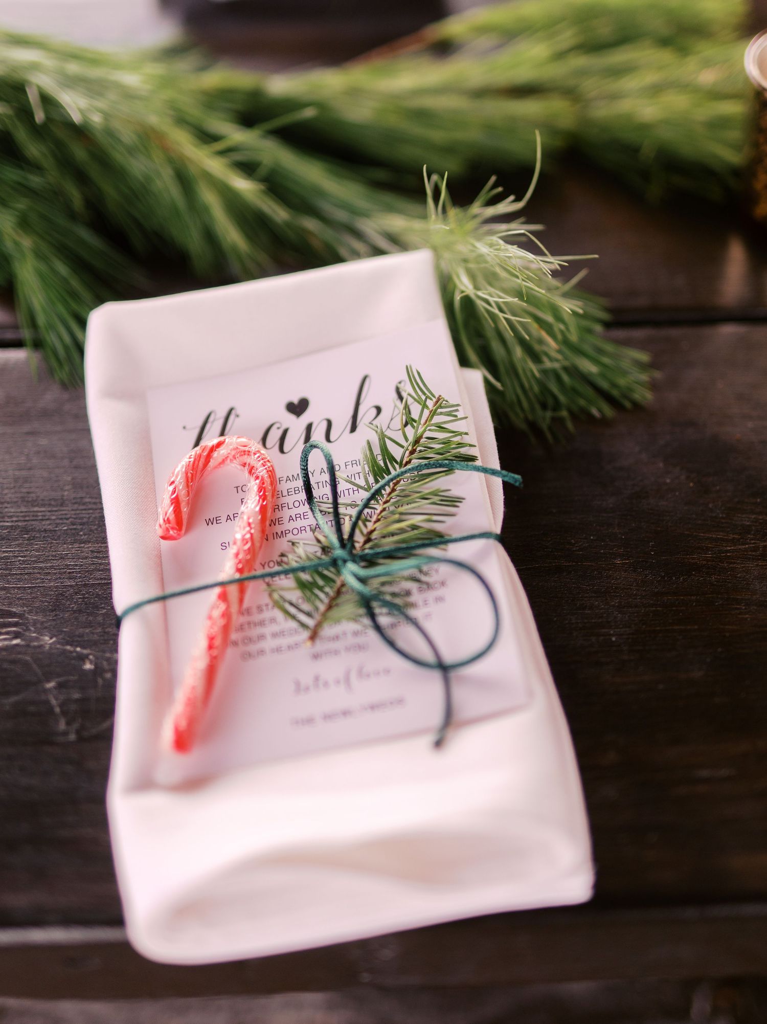 White ceramic dish with candy cane and evergreen sprig tied with twine on dark wooden surface.