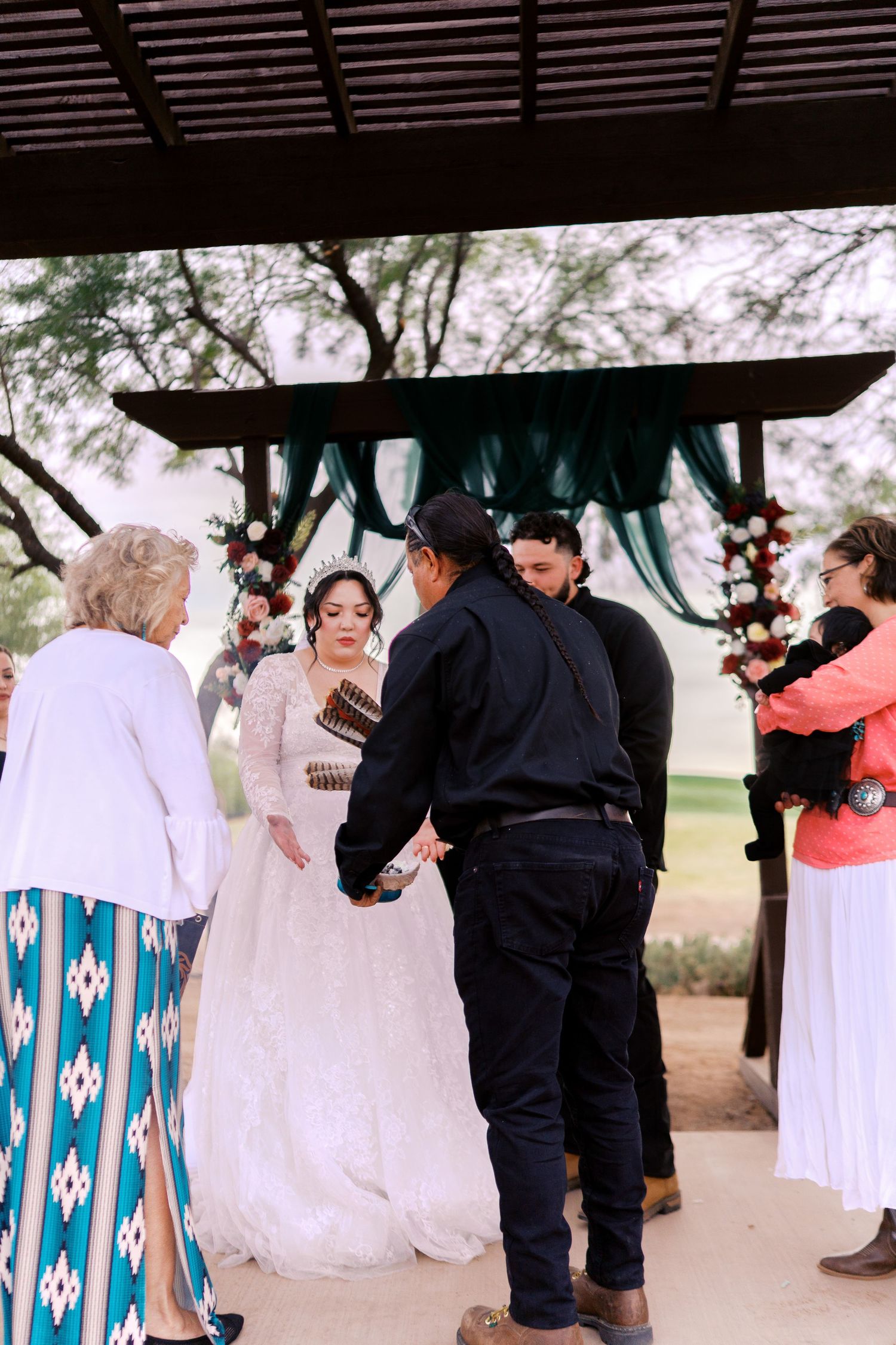 An outdoor wedding ceremony takes place under a covered pavilion with teal drapery and decorative accents.