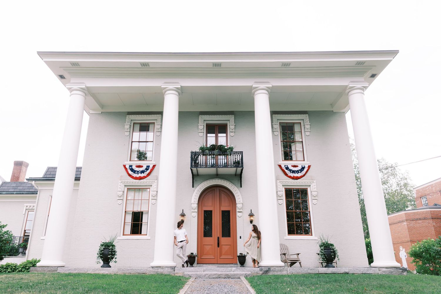A historic white colonial building with elegant columns and an American flag draped on its front porch.