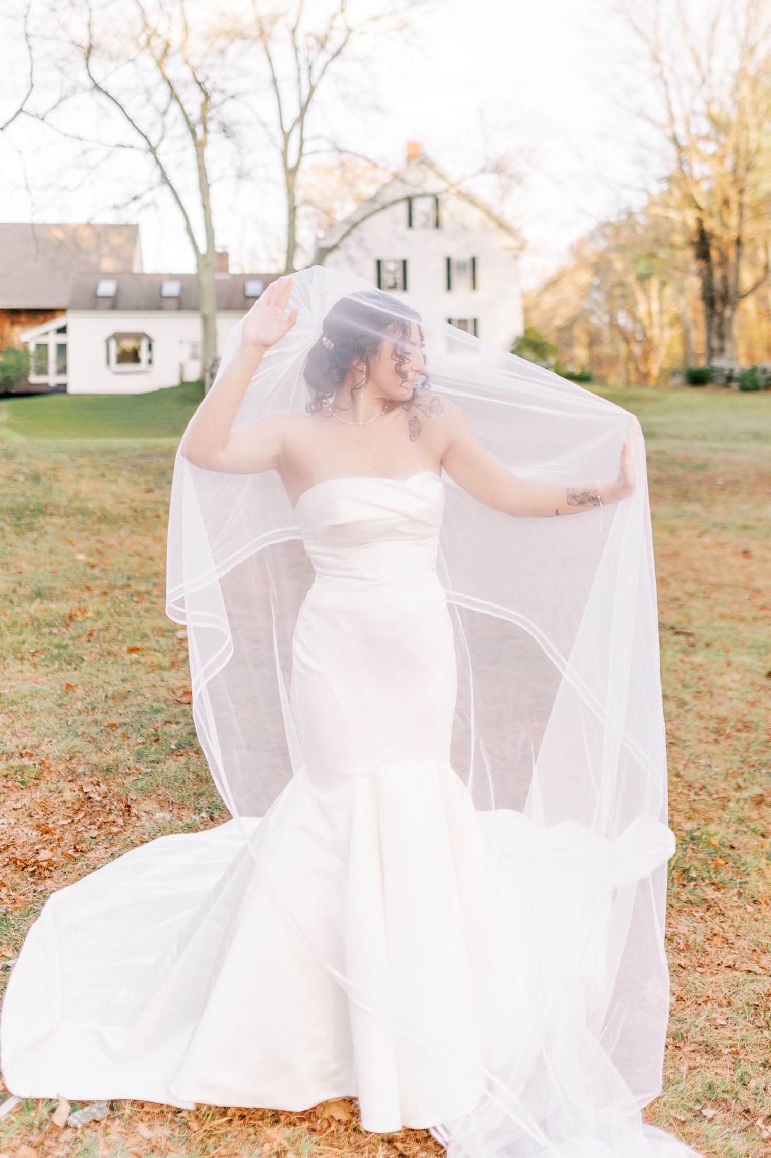 A bride in a white wedding dress twirls gracefully in an autumn field with fallen leaves.