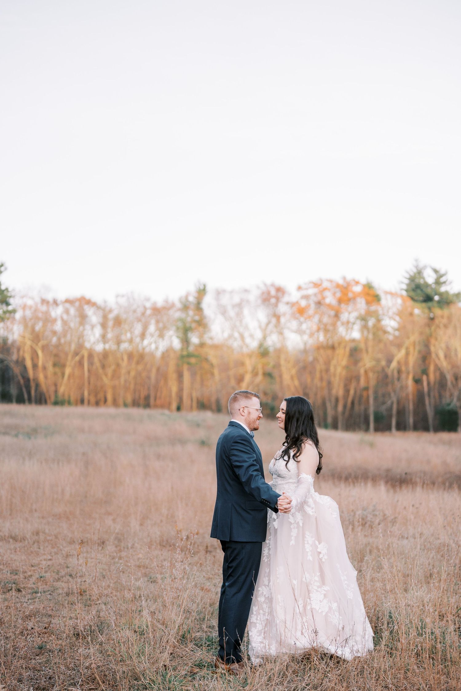 A couple in wedding attire shares intimate moments in a golden autumn field during their outdoor photoshoot.