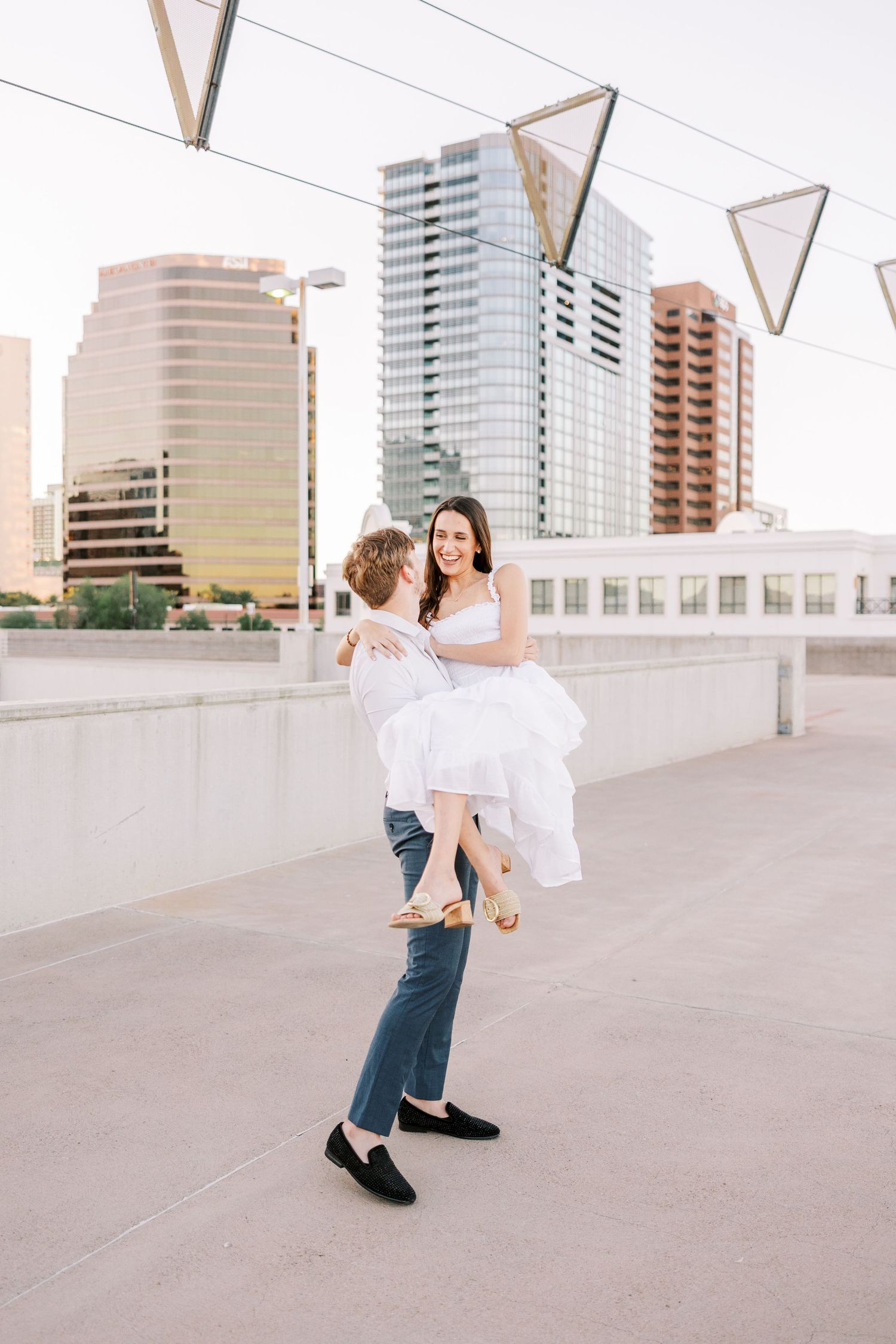 Couple in white and denim dancing on rooftop with city skyline backdrop.