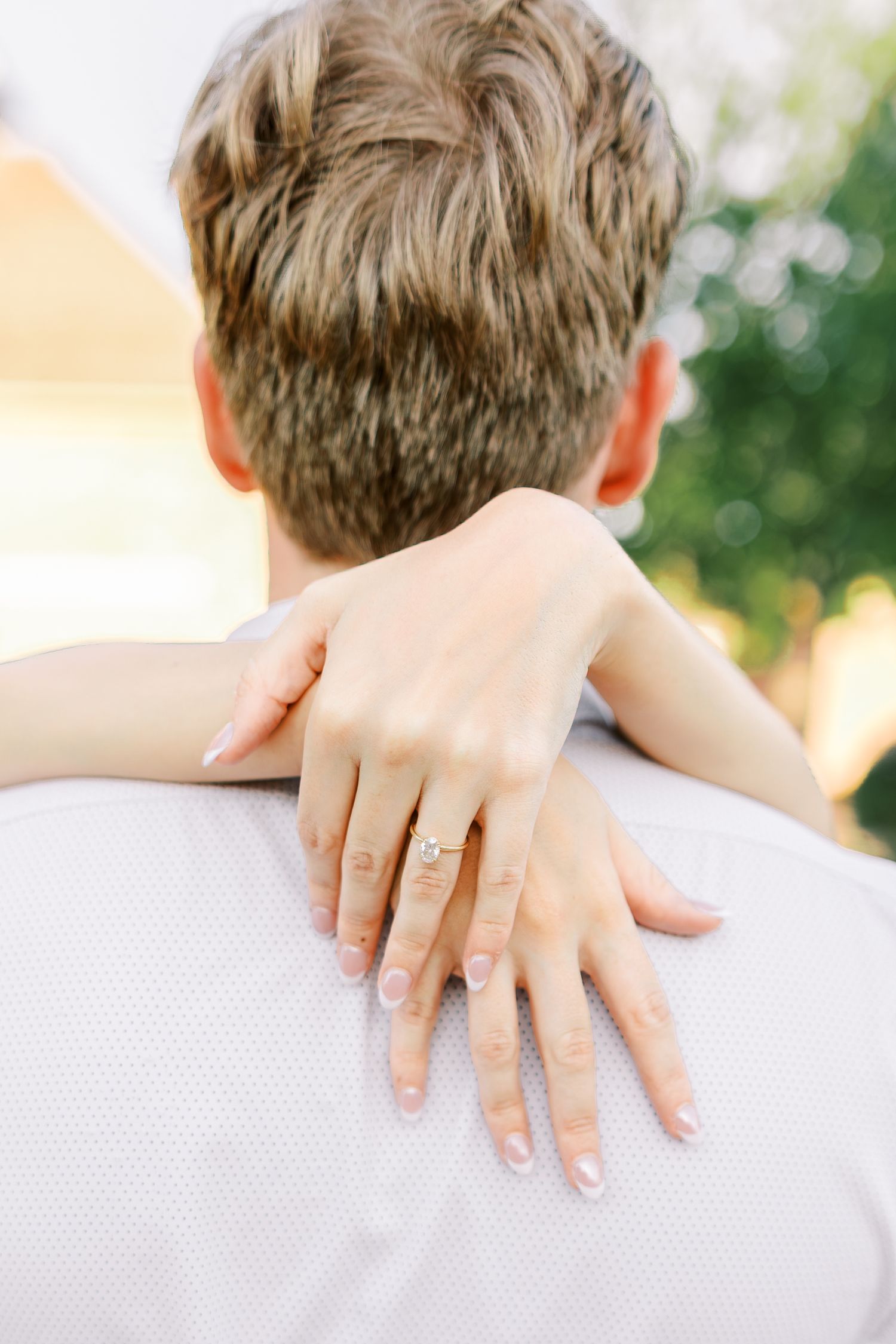 Close-up shot of hands displaying an engagement ring against a white background.