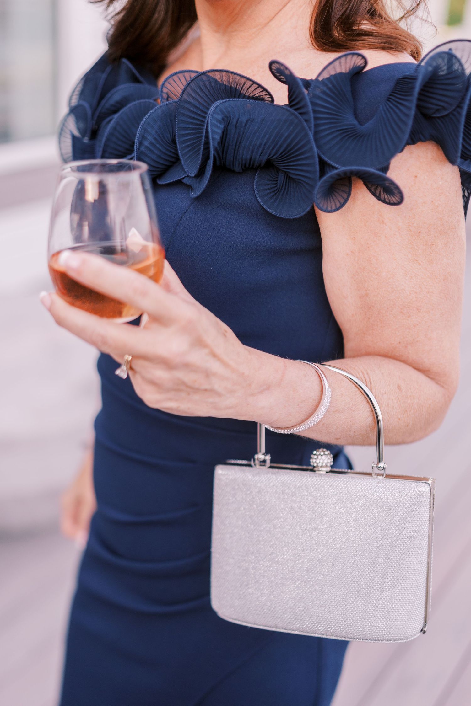Navy blue dress with ruffled sleeves paired with silver clutch purse and wine glass accessories.