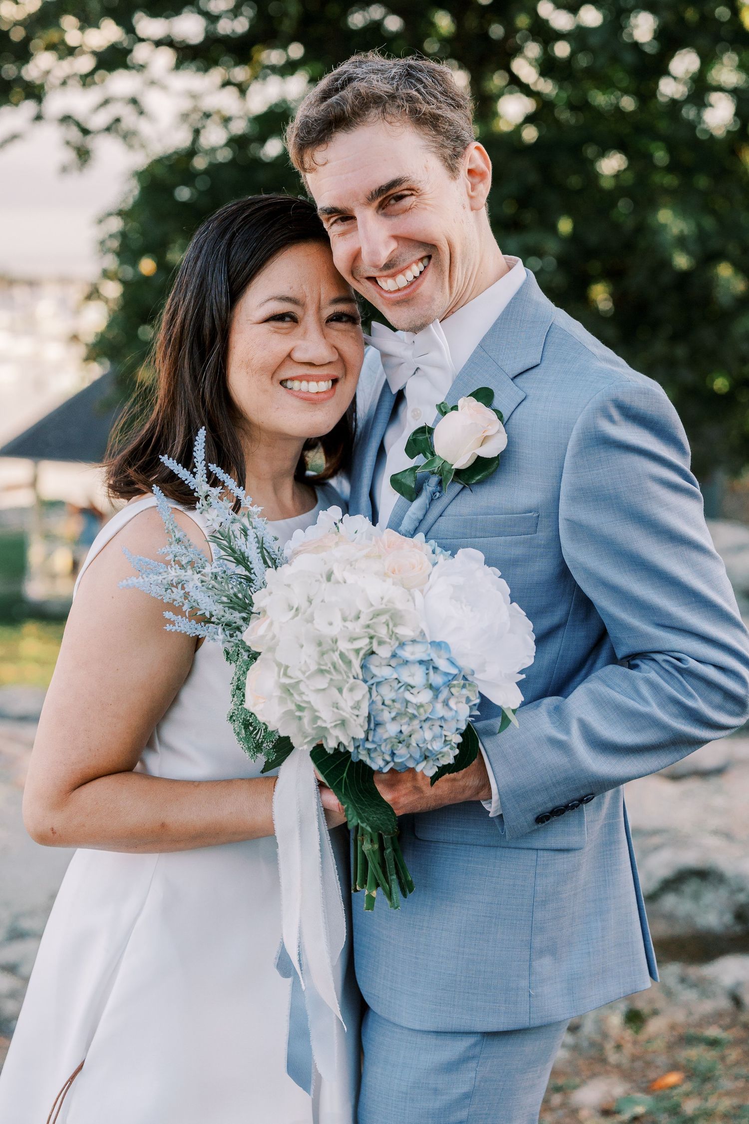 A romantic wedding portrait with light blue and white floral bouquet against a natural backdrop.