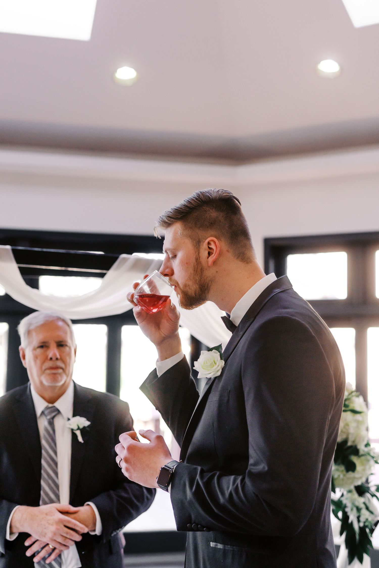 A suited guest takes a sip of wine during an elegant indoor wedding reception.