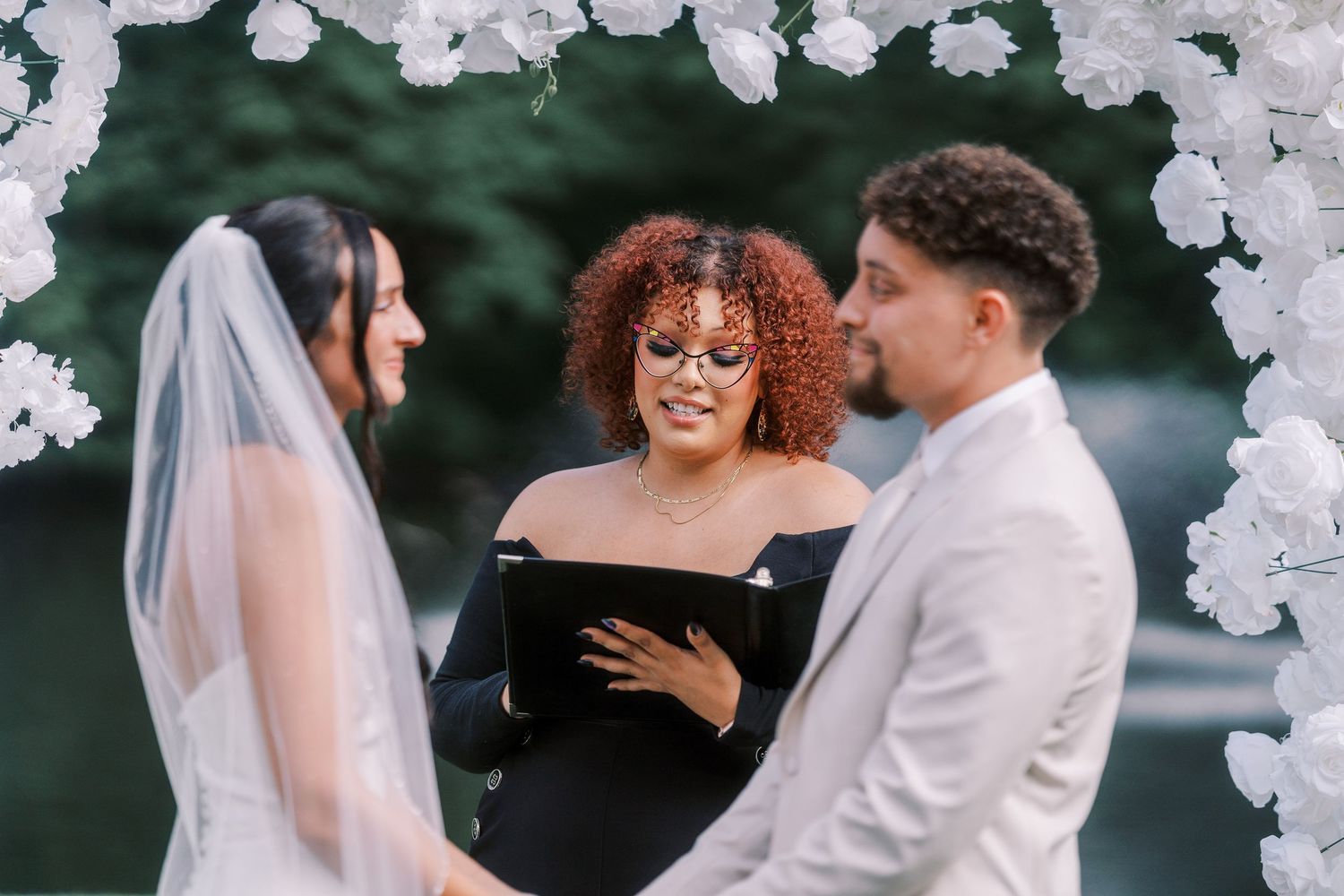 Wedding ceremony under white floral arch with officiant and couple.
