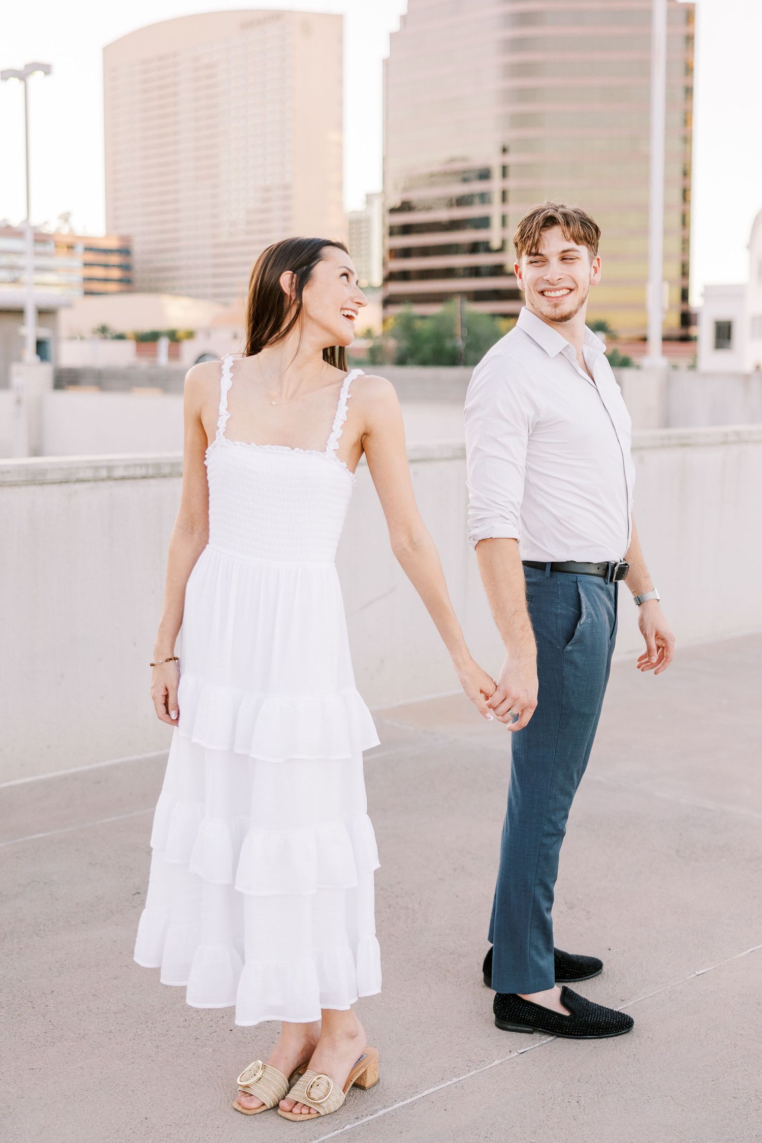 A couple in white and navy outfits walking and laughing together in a bright urban environment.