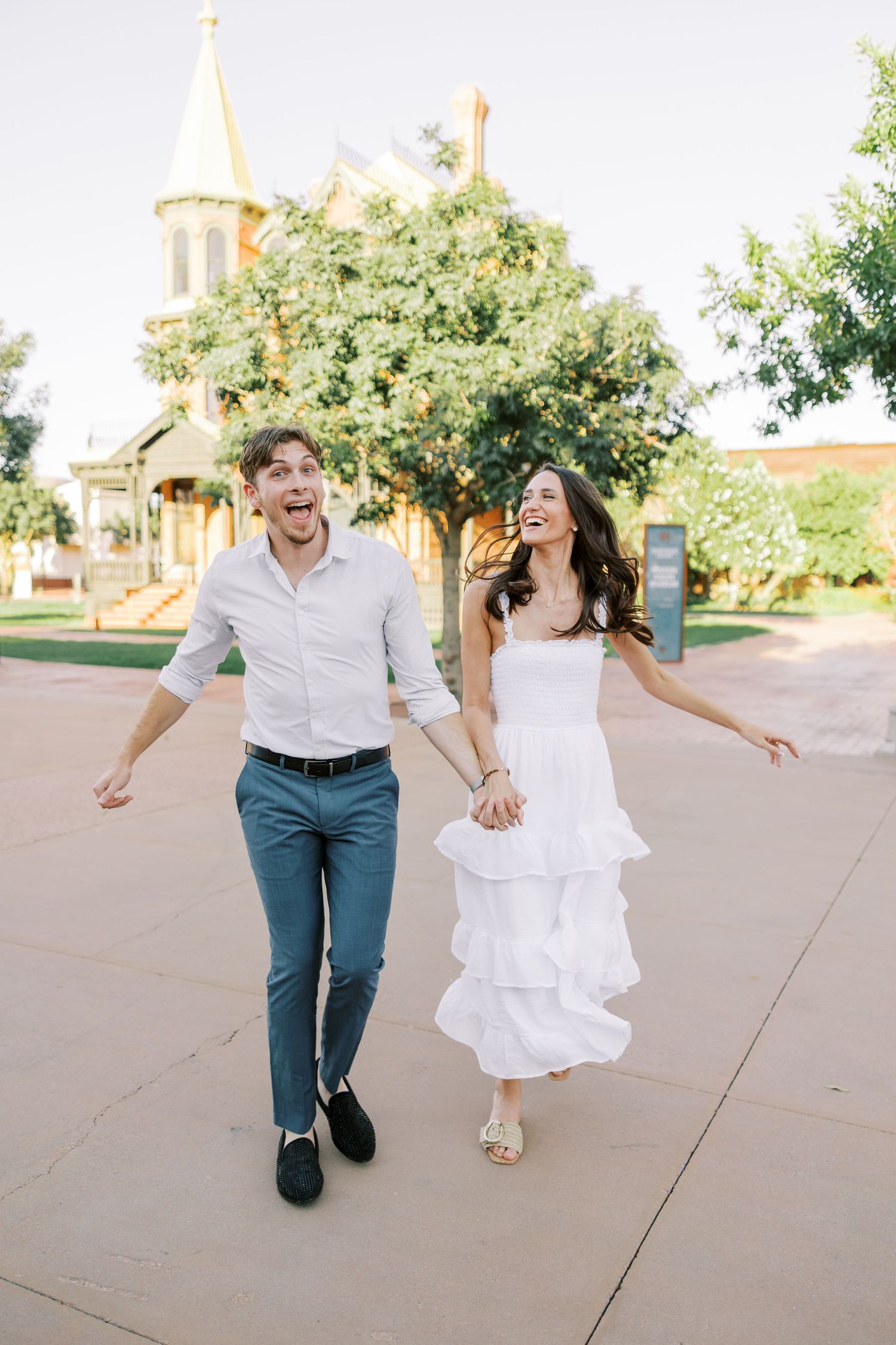 Joyful couple running and dancing together outdoors on a sunny day near a church building.