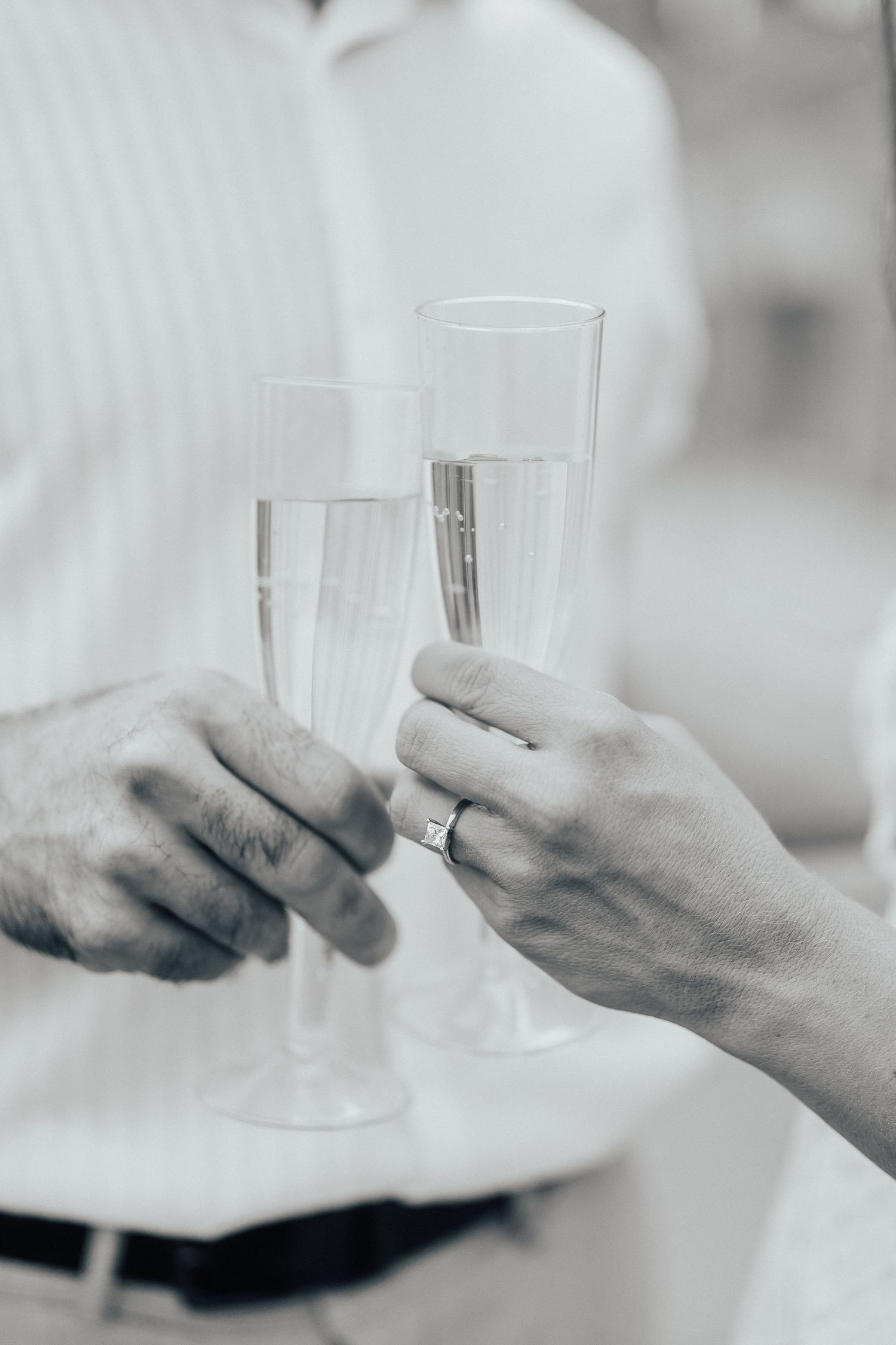 Two hands hold champagne glasses in a black and white photo.