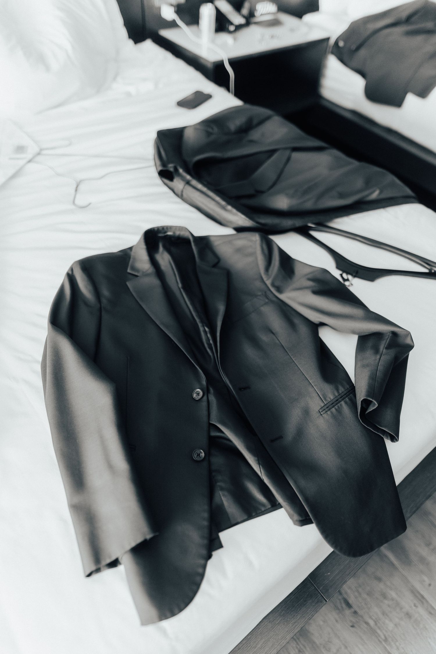 A sleek black leather blazer jacket lying on white bedding with clean modern styling.