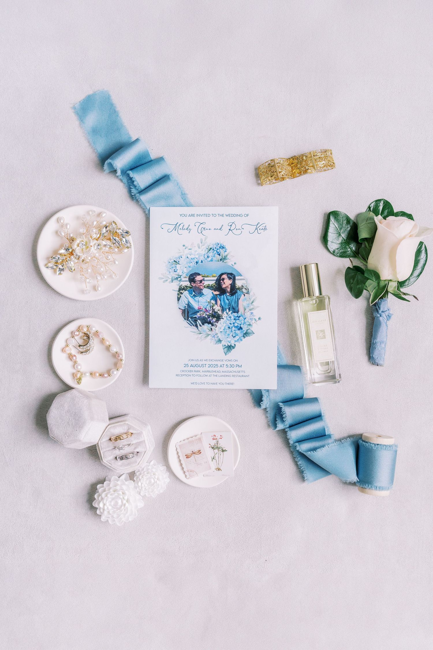 Wedding accessories flatlay with blue ribbons, invitations and decorative elements on white background.