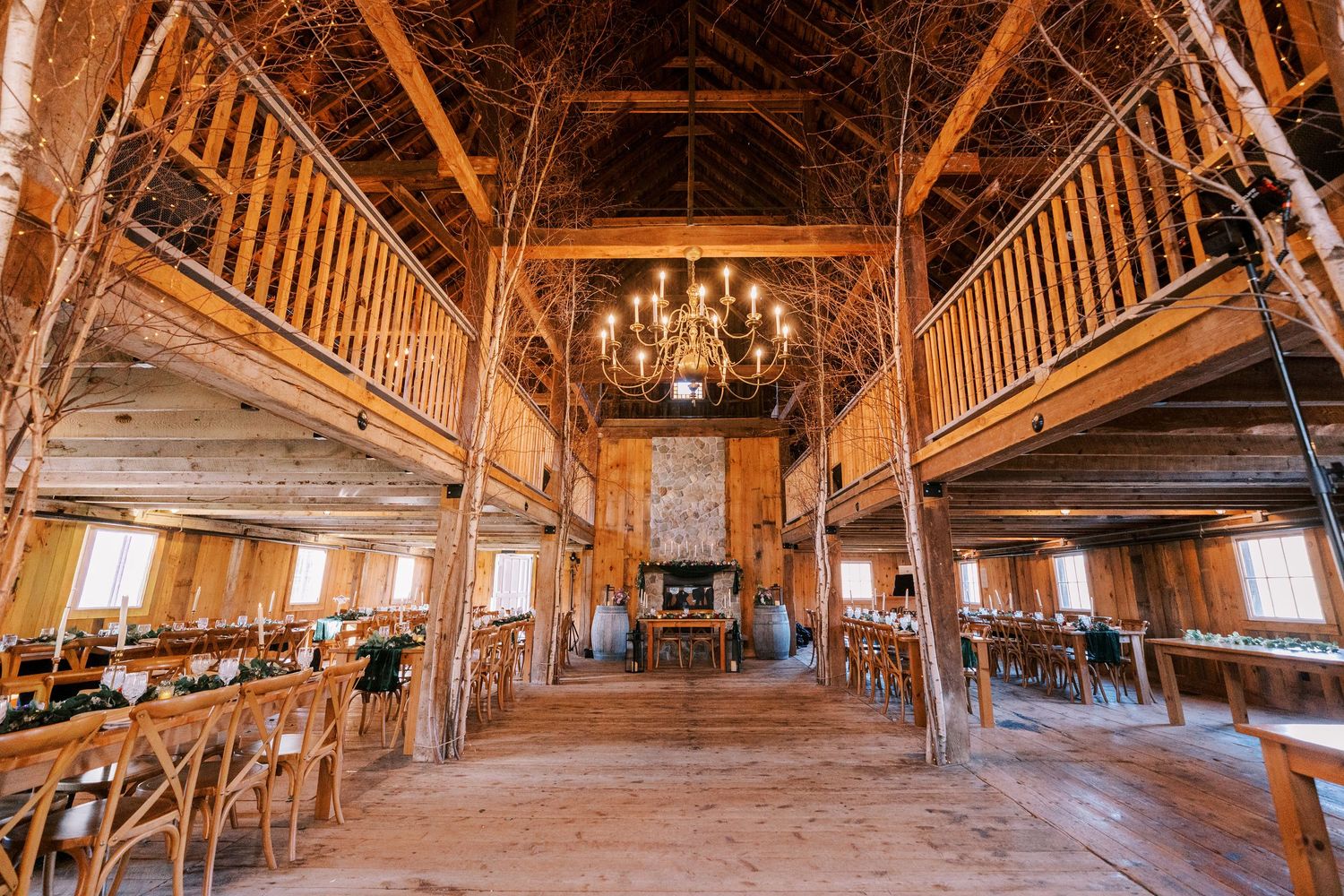Panoramic view of a rustic wooden barn interior with exposed beams and natural light streaming through windows.