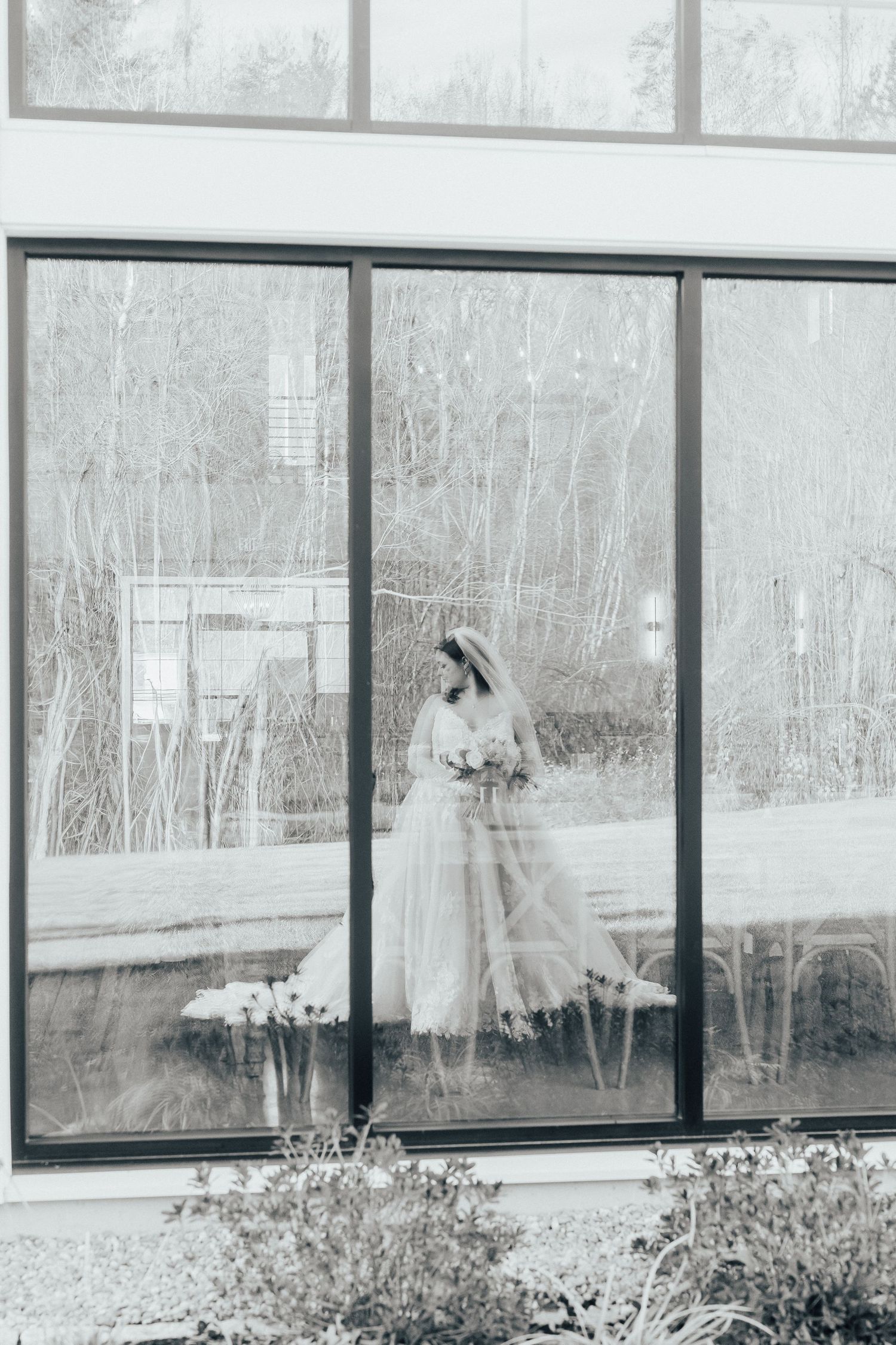 Black and white photograph of a greenhouse with windows reflecting winter scenery and snow outside.