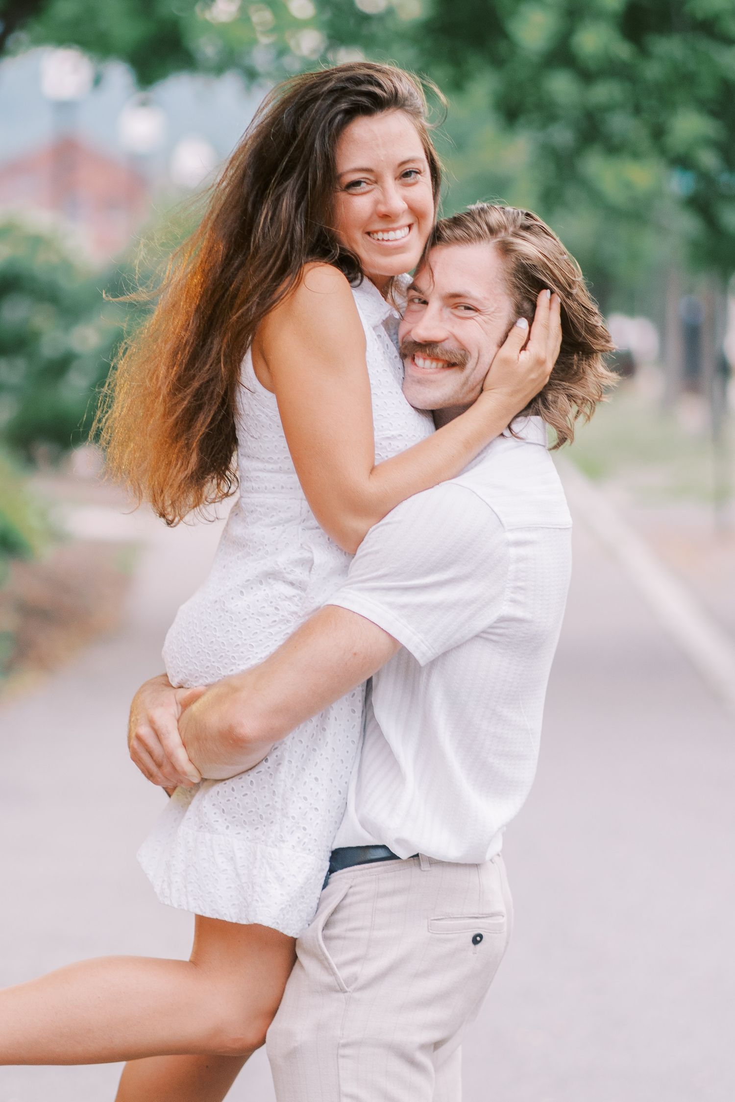 A joyful embrace captured on a tree-lined street during a summer photoshoot.