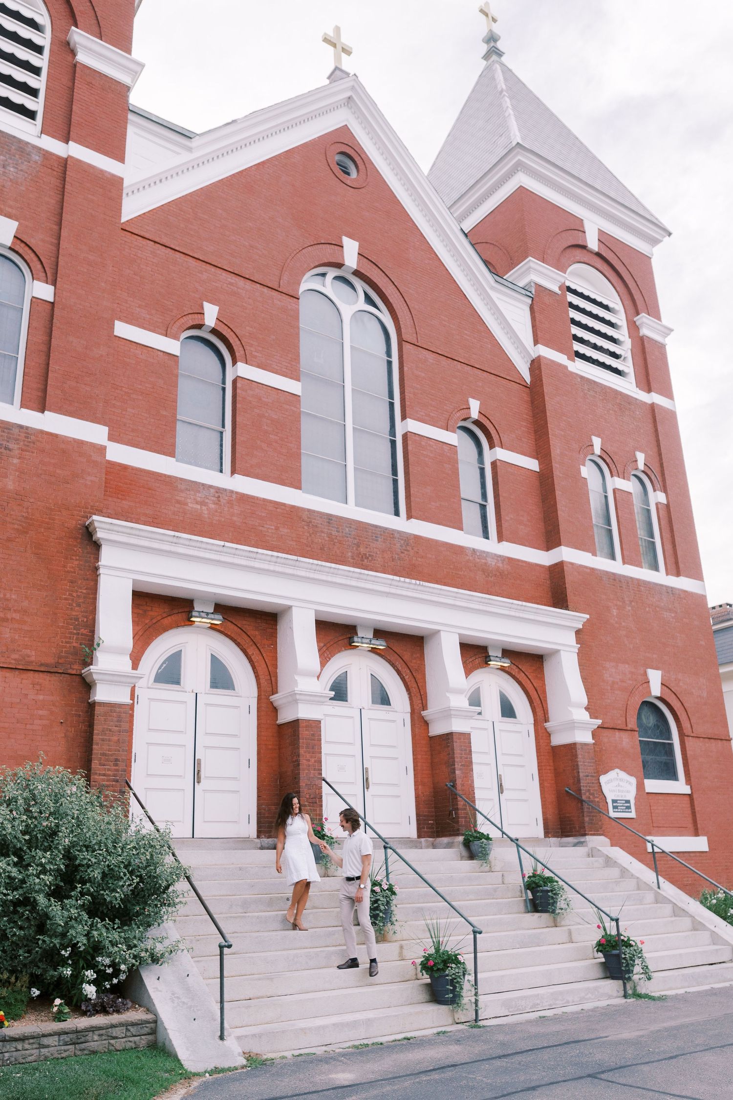 A red brick church with white trim and multiple crosses on top of a steep stairway entrance.