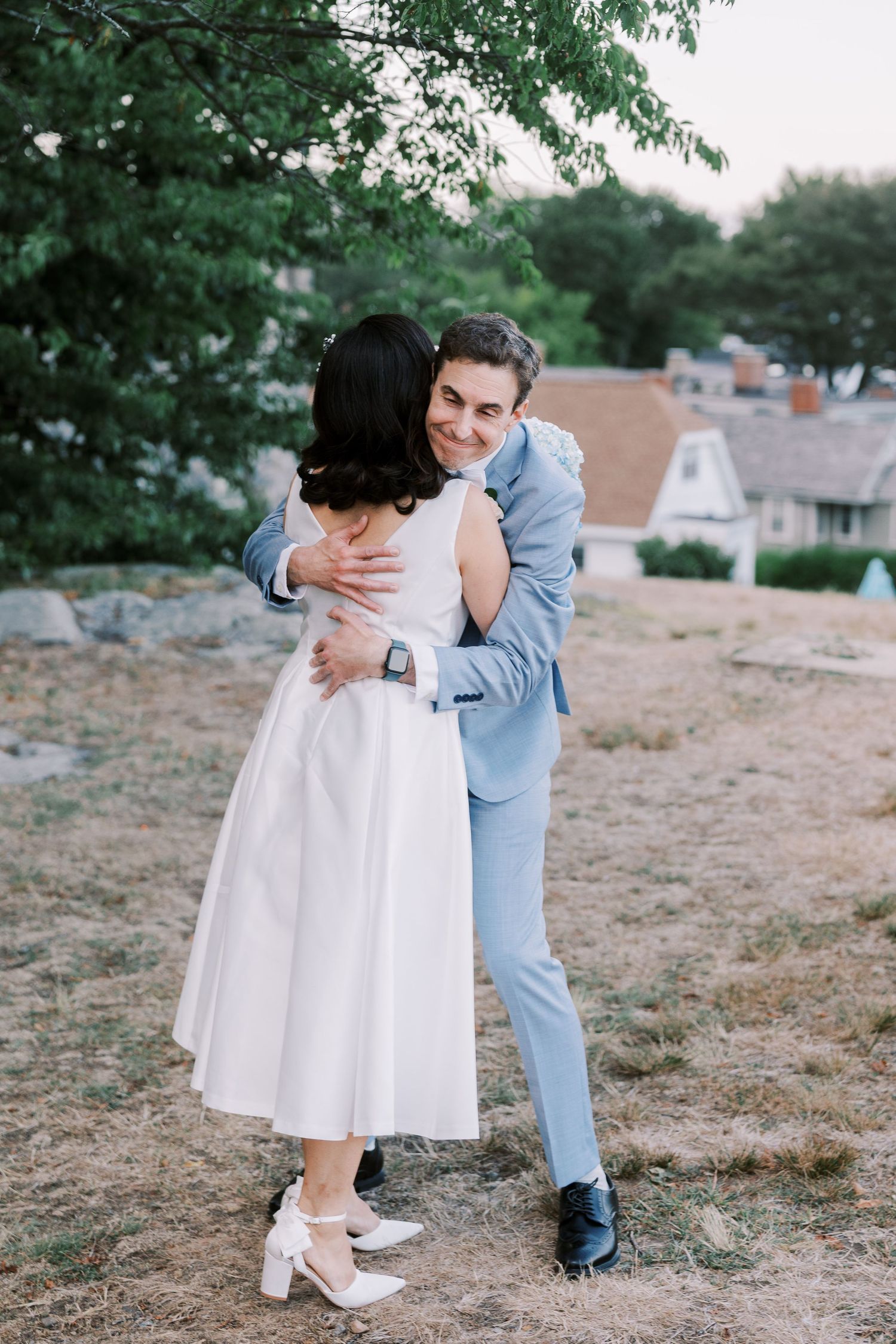 A couple poses for artistic first look wedding photos on grassy outdoor terrain.