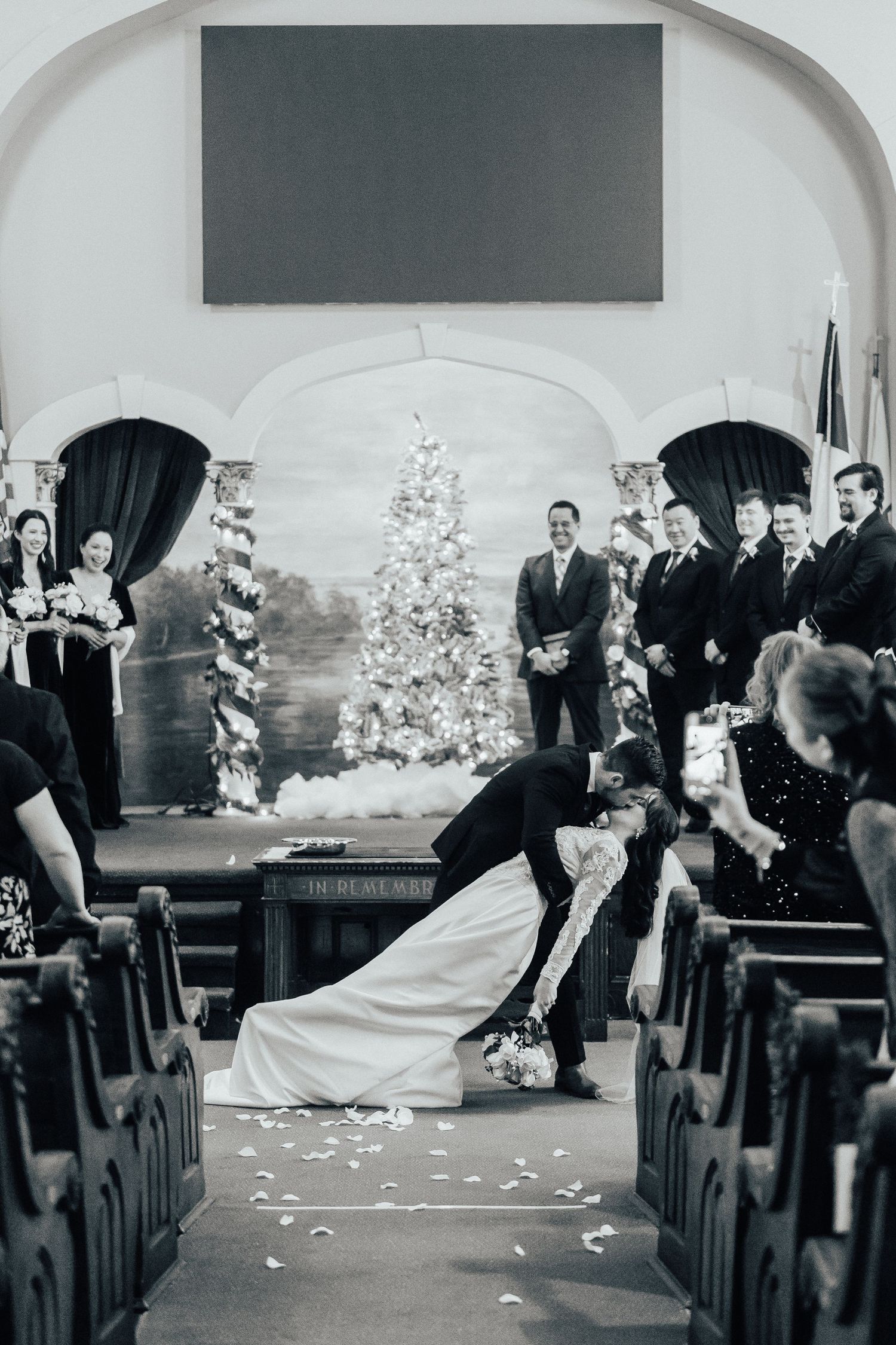 Black and white photo of wedding celebration with flower petals being tossed in church aisle.