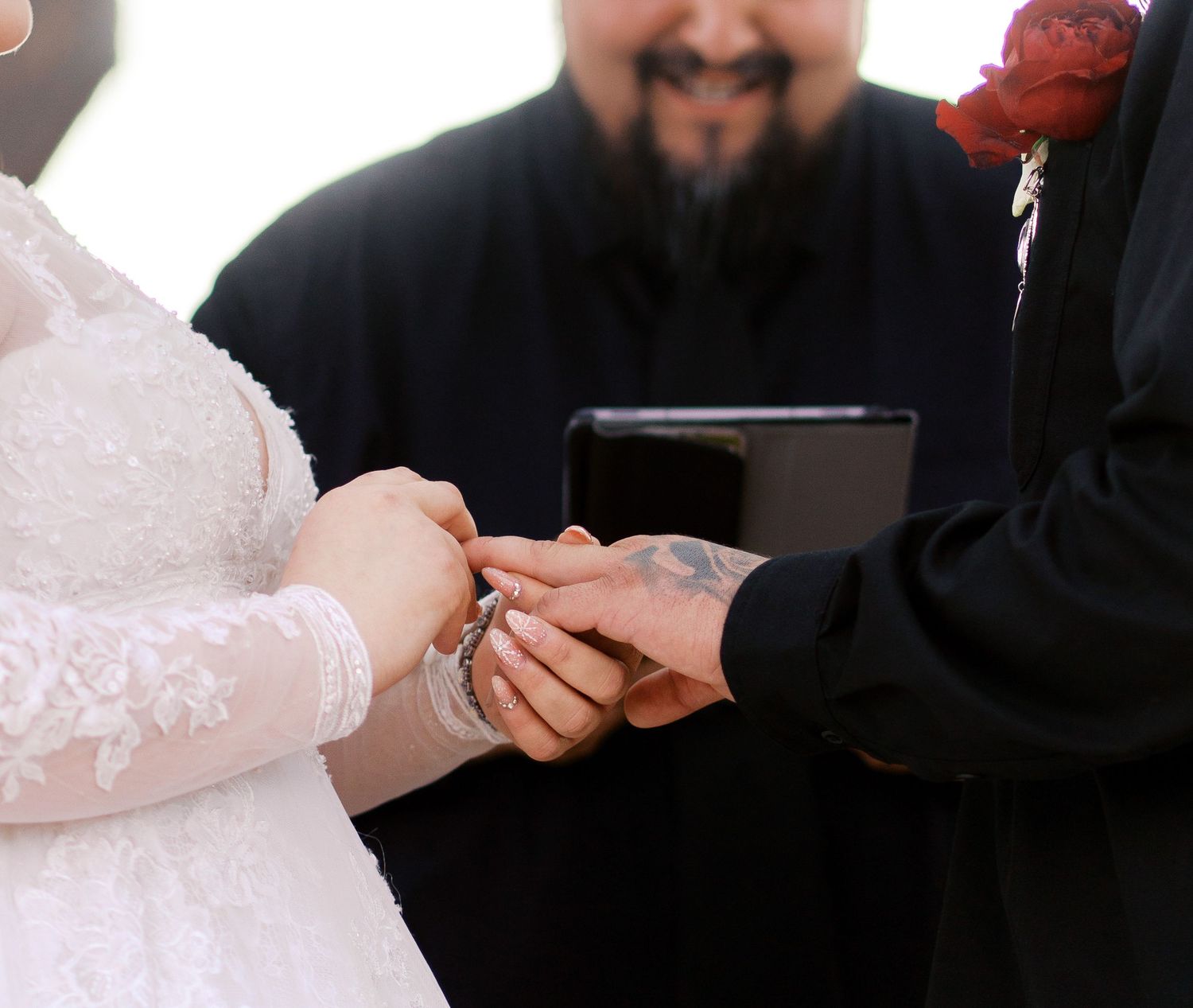 Close up of hands exchanging rings during a wedding ceremony with white lace sleeves visible.