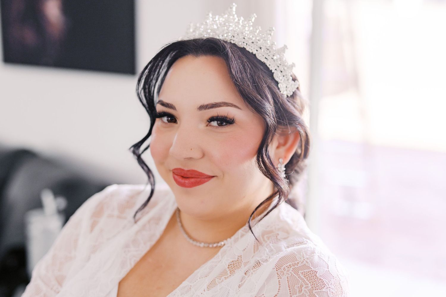 Bride wearing sparkly tiara and white robe smiles while getting ready for wedding ceremony.