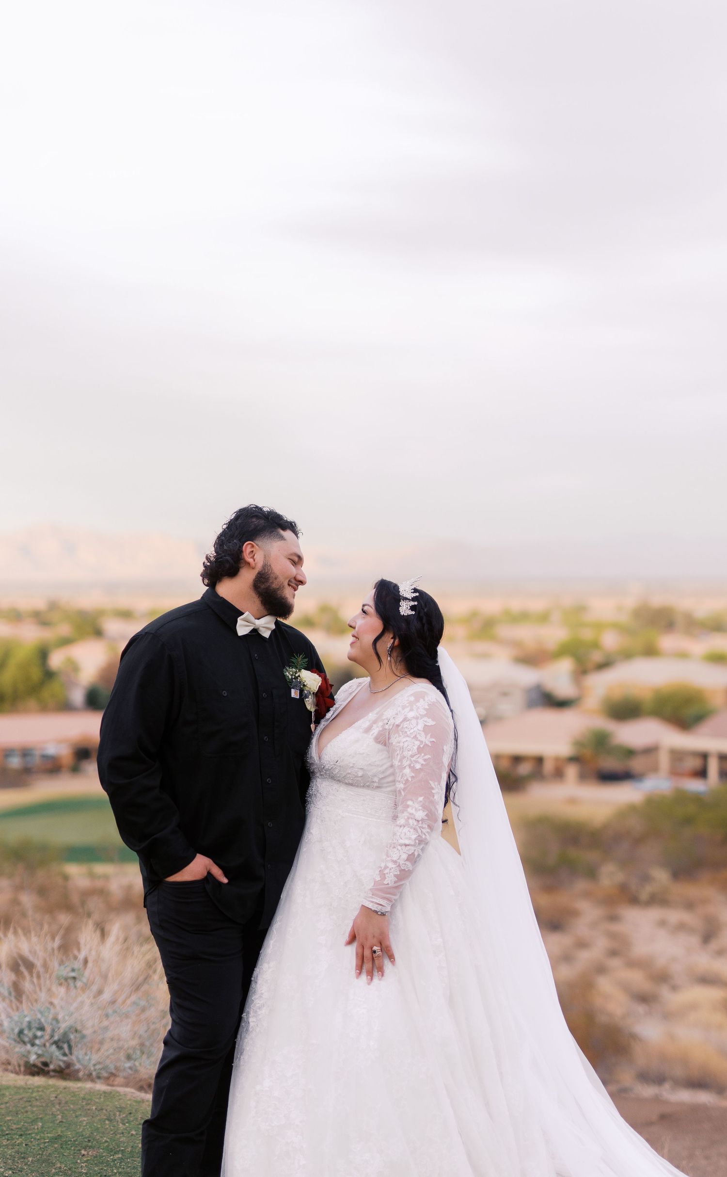 A bride and groom share a joyful moment together on a desert hilltop during their wedding photoshoot.