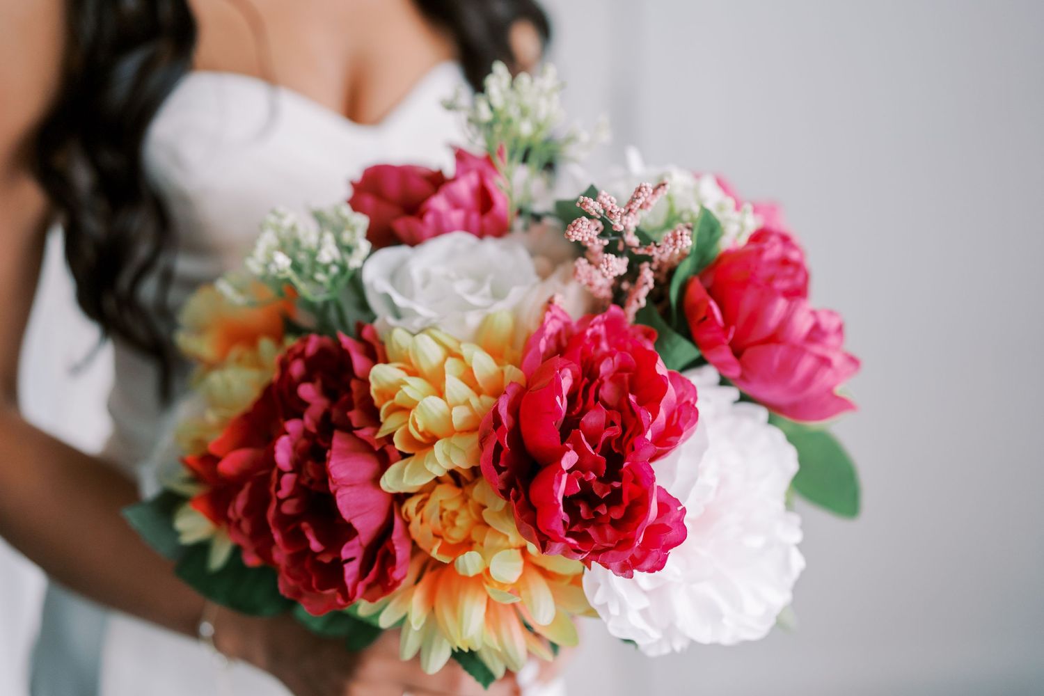 Vibrant pink and white wedding bouquet featuring peonies and dahlias against a white bridal gown background.