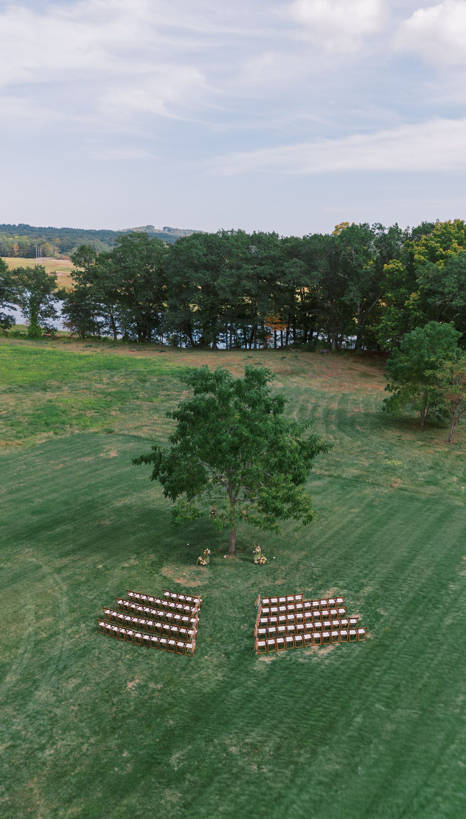 Aerial view of outdoor wedding ceremony setup with wooden chairs arranged in a chevron pattern on a green lawn.
