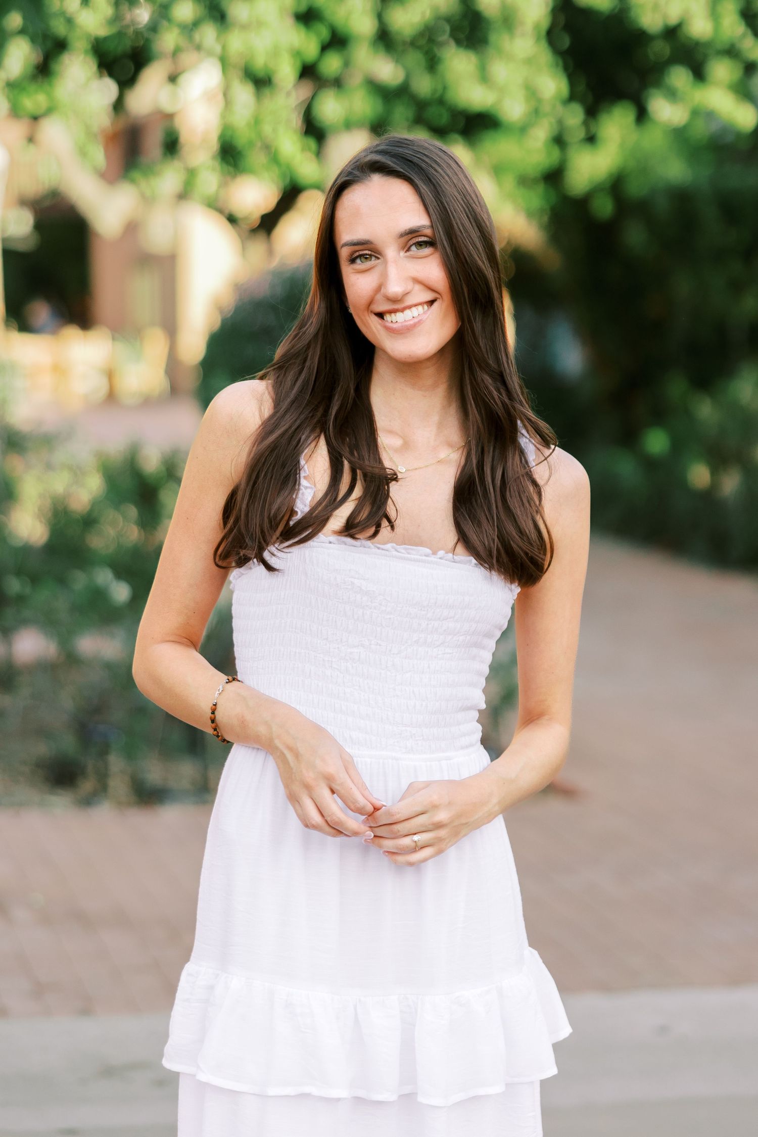 Woman in a white summer dress poses outdoors with a bright smile against a natural background.