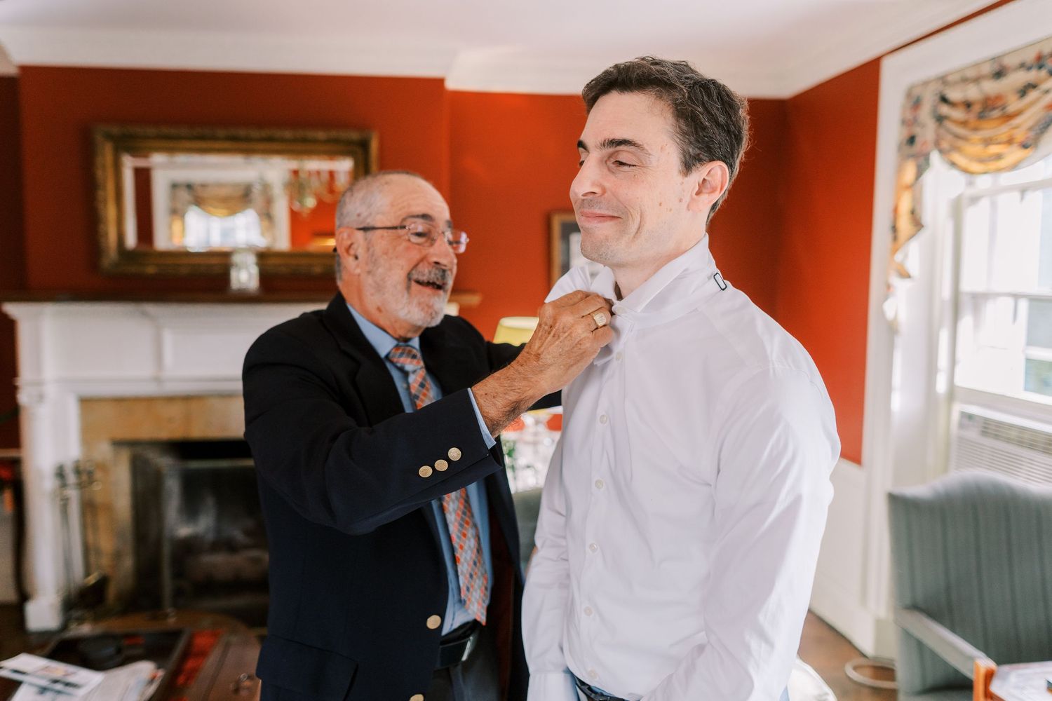 Getting ready for a special occasion in a red-walled room with someone helping adjust formal attire.