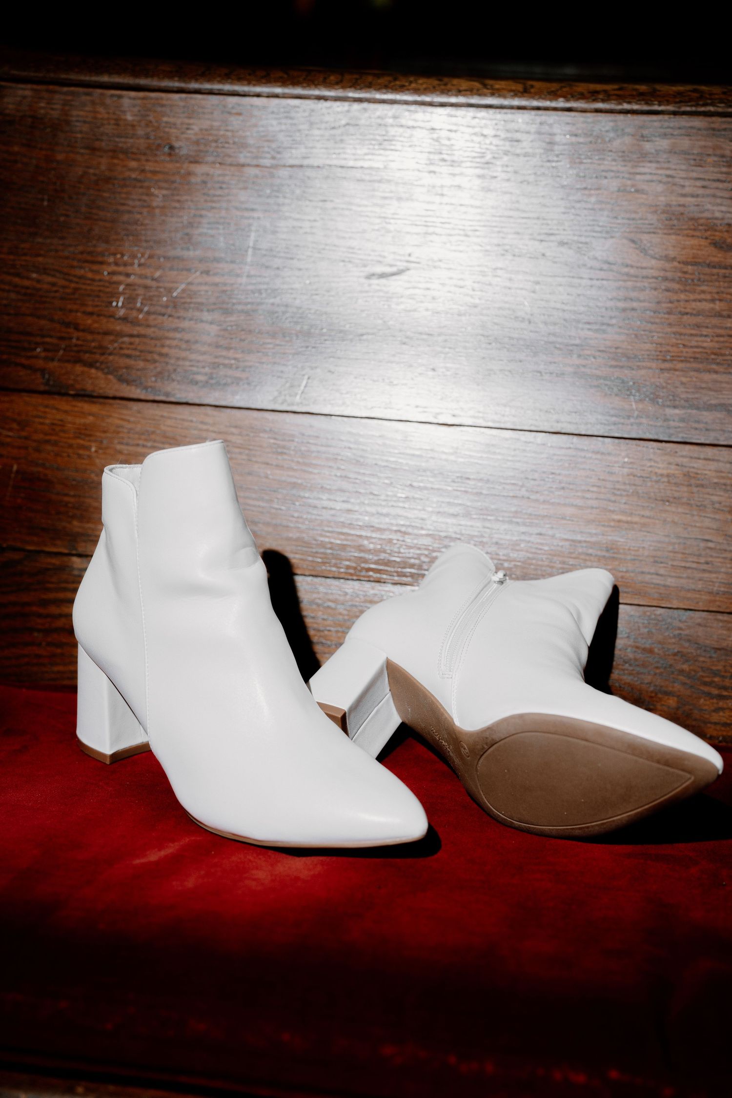 White and beige wedding shoes displayed on a dark wooden surface with red velvet.