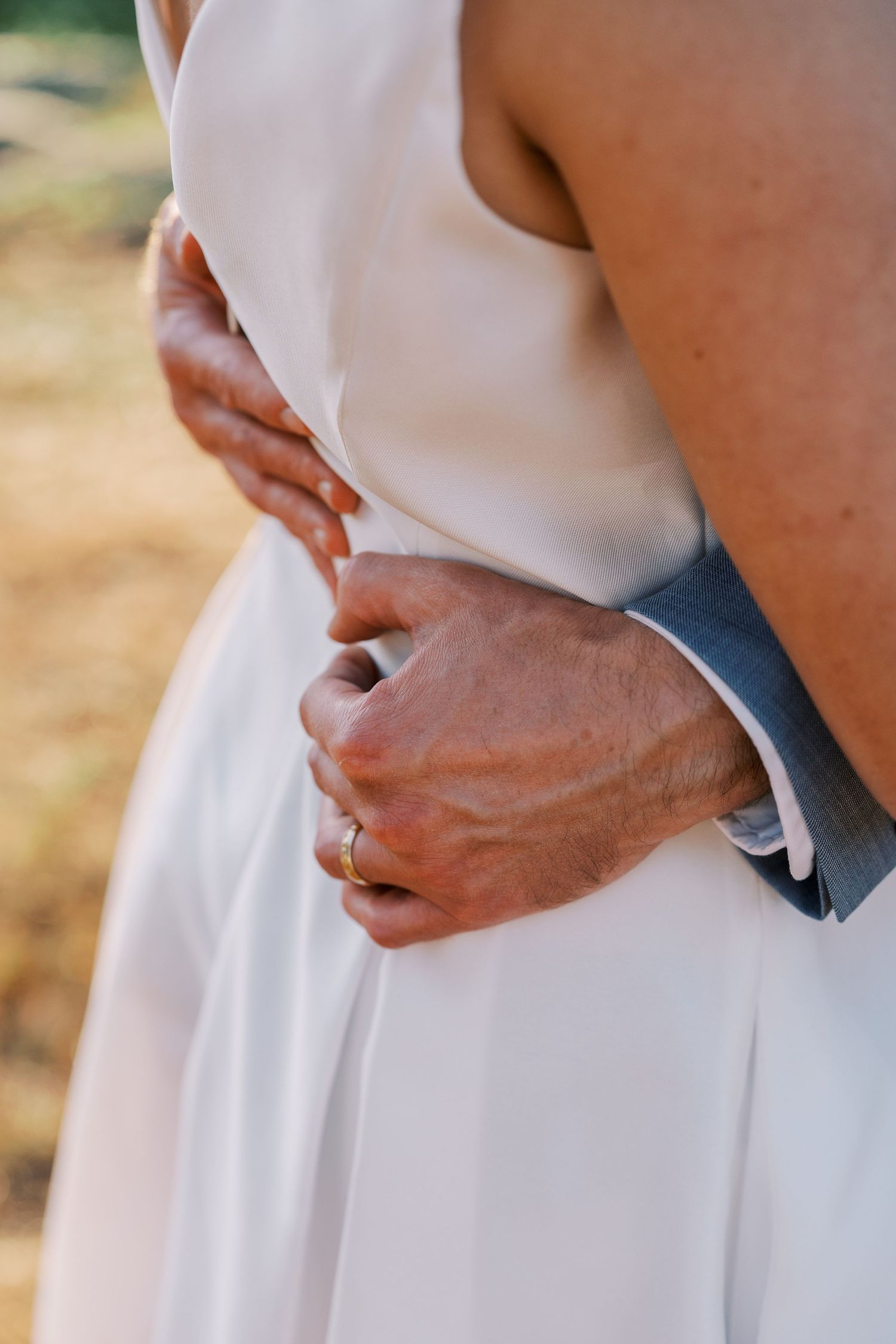 Close-up detail shots of hands holding the waist of a white wedding dress.