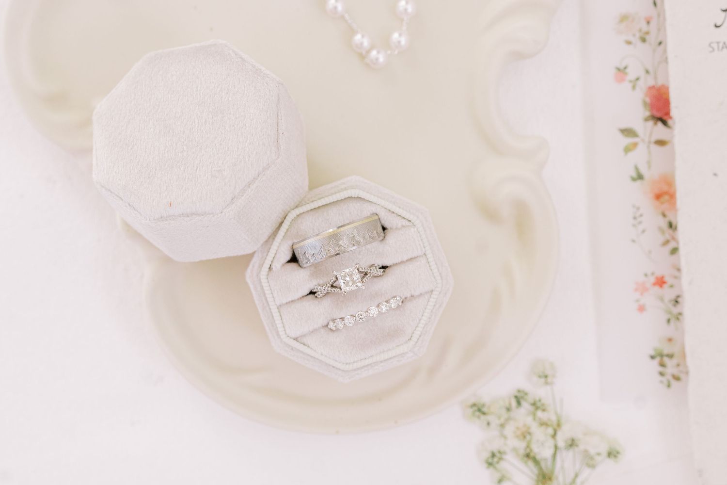Elegant white wedding invitations and floral decor arranged on a light beige surface with delicate details.
