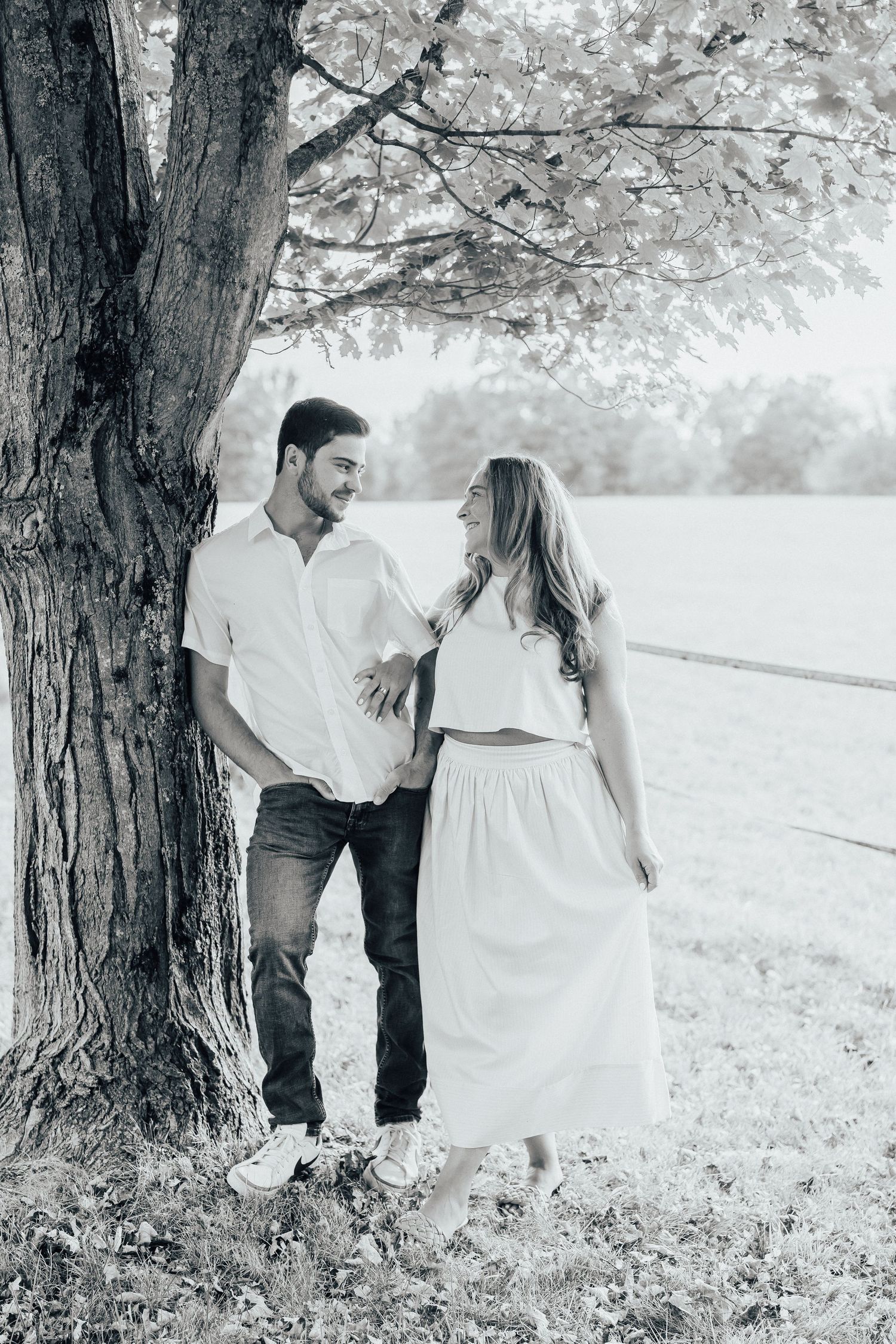 A tender moment captured under a large tree in black and white photography.